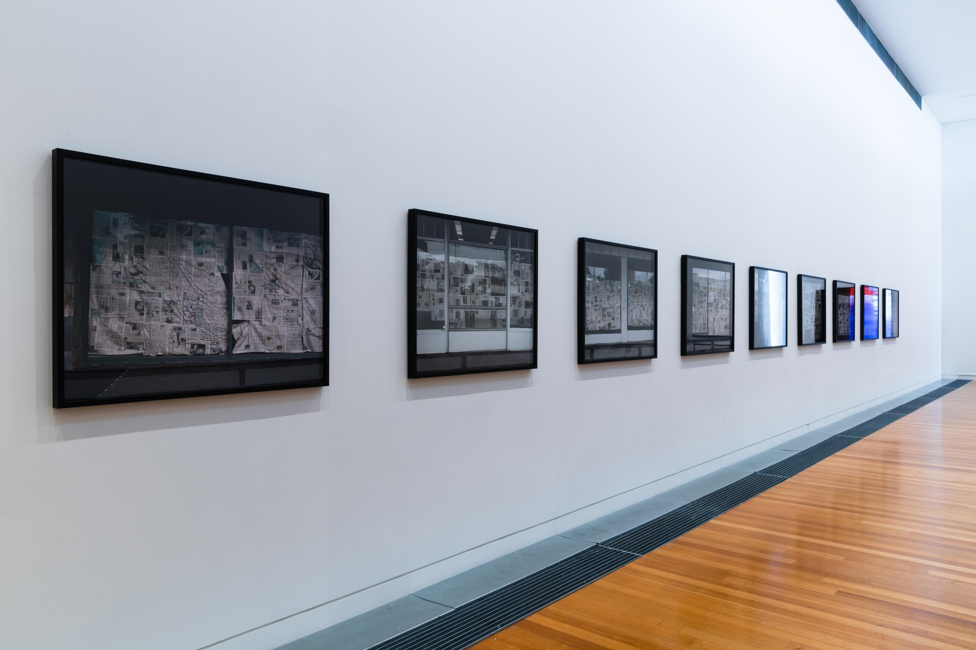 a row of framed black and white photographs of shop fronts with newspaper on their windows