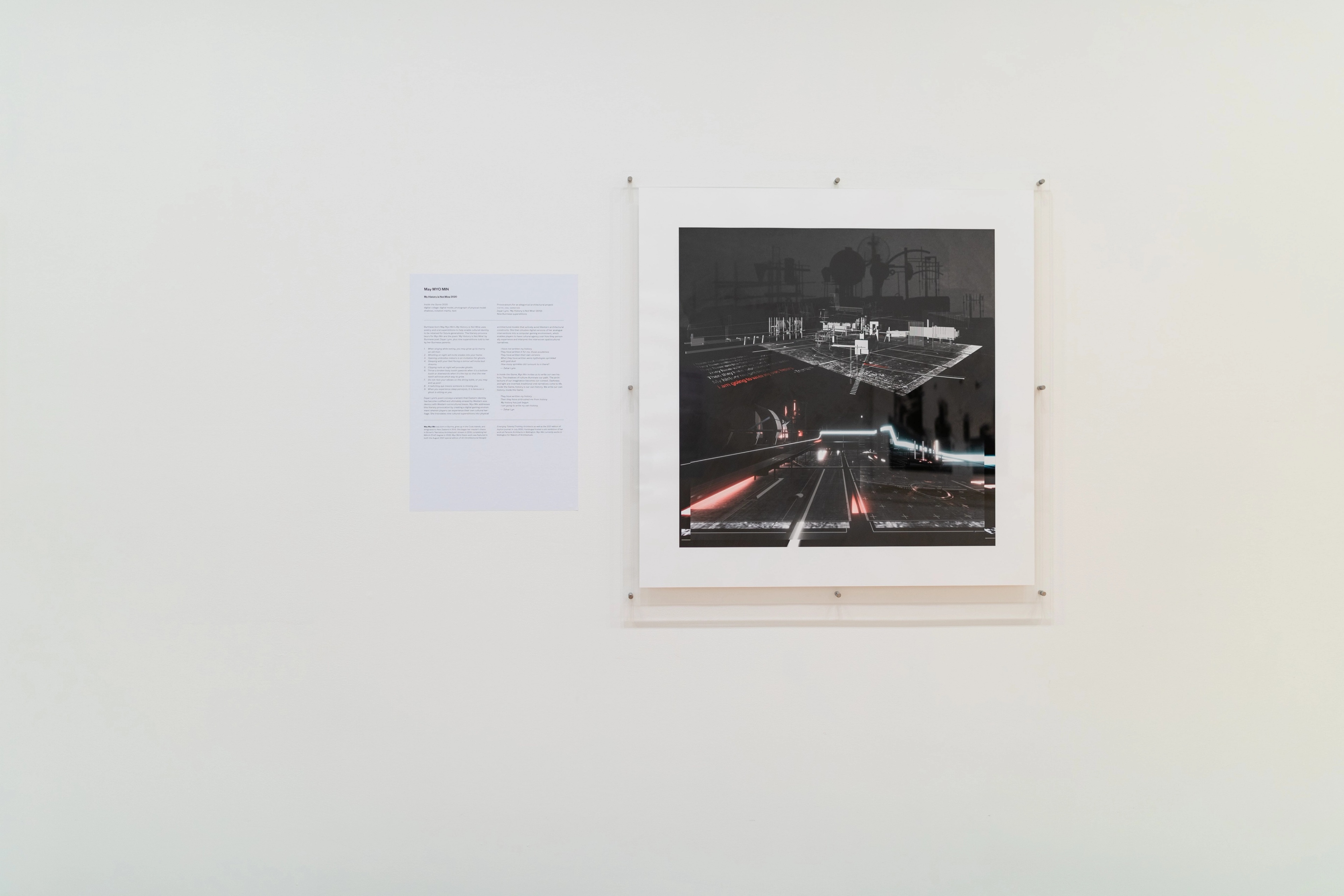 Straight on view of a gallery wall with text and a square architectural image in a perspex mount. Daniel K. Brown