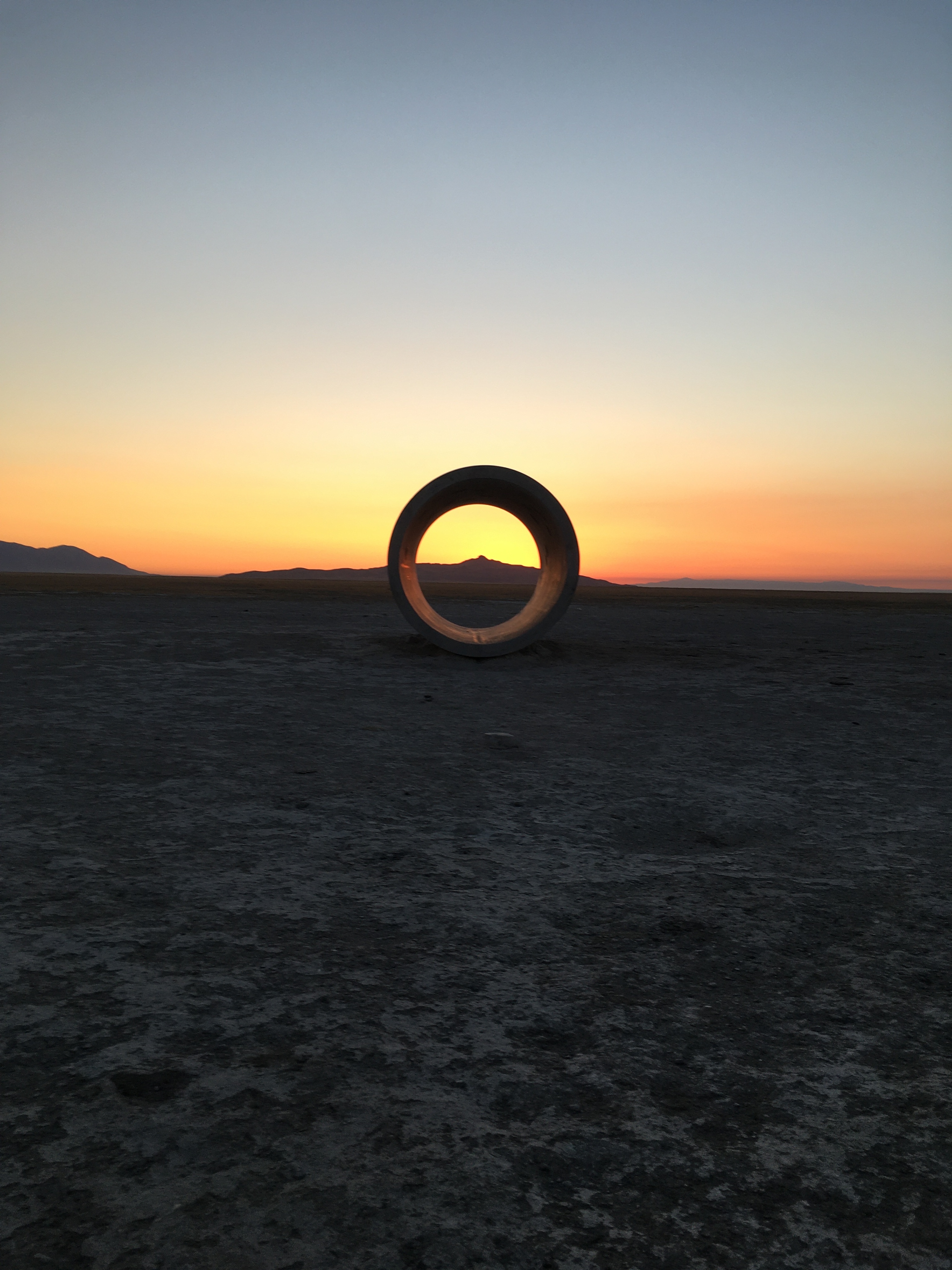 Landscape with sunsetting, large tunnel sculpture framing is central in the frame framing a peak in the distance. 