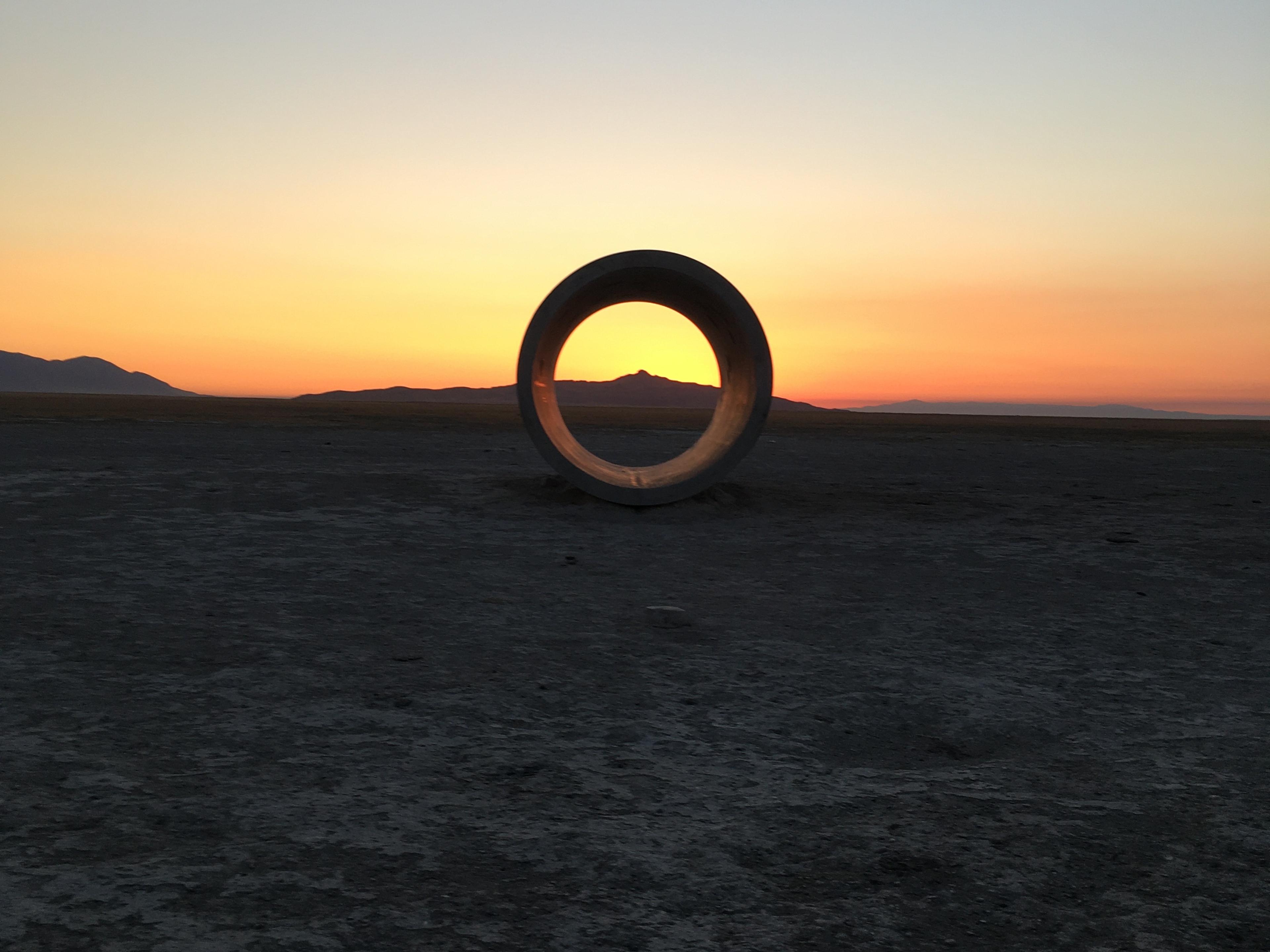 Landscape with sunsetting, large tunnel sculpture framing is central in the frame framing a peak in the distance. 