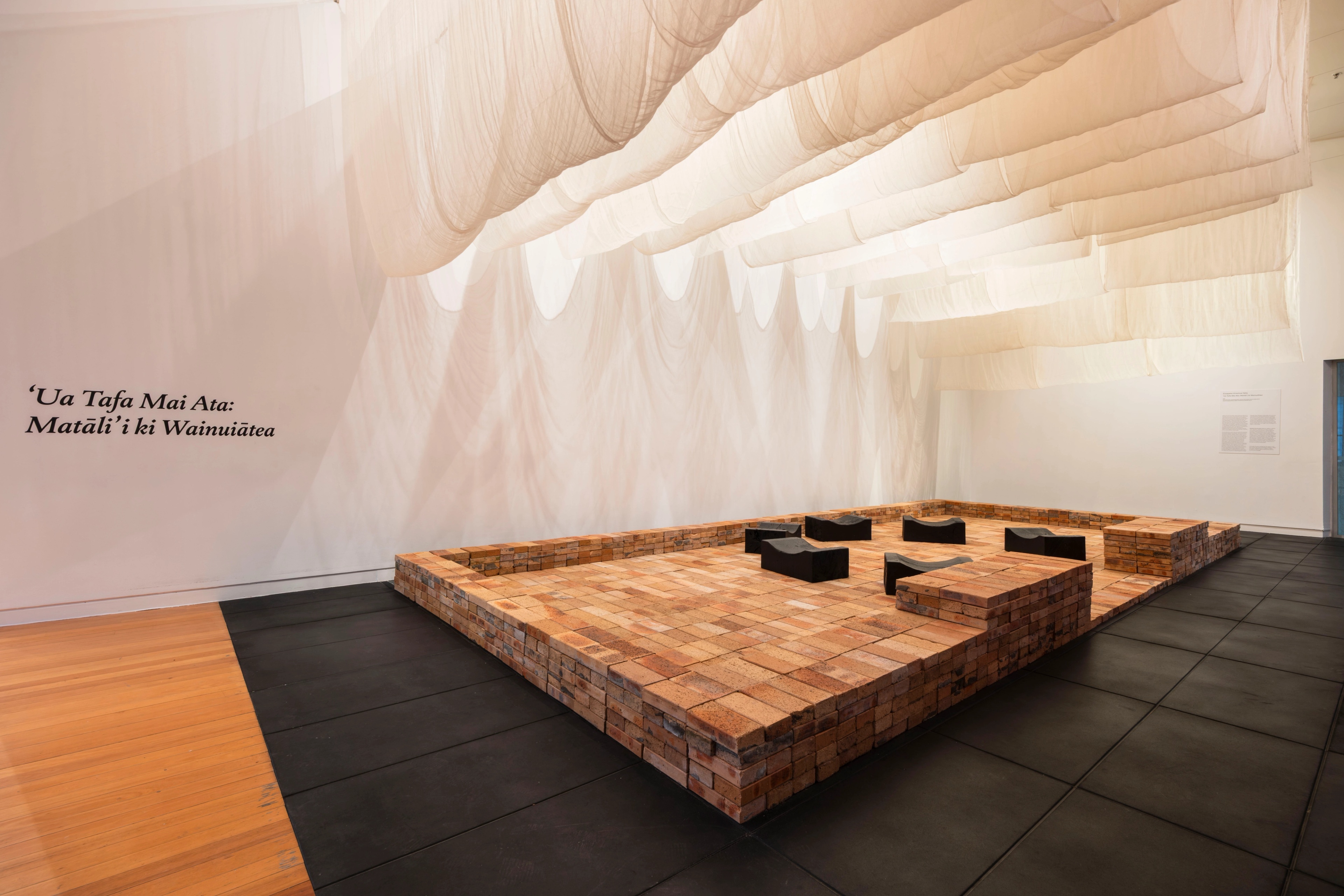A brick platform, with six black benches on it, and draped fabric suspended above.