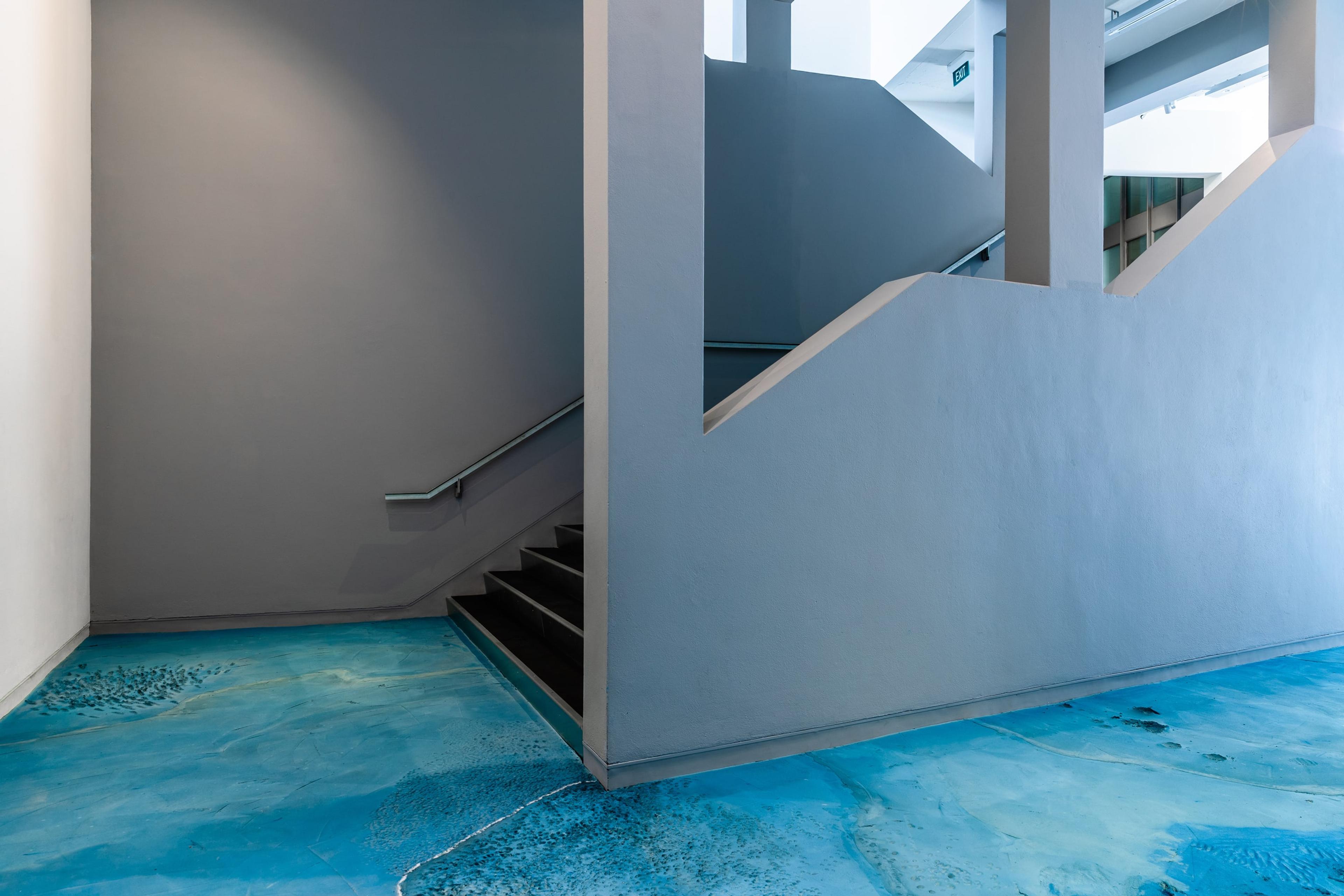 A view of a staircase in the gallery with grey walls and a textured blue floor