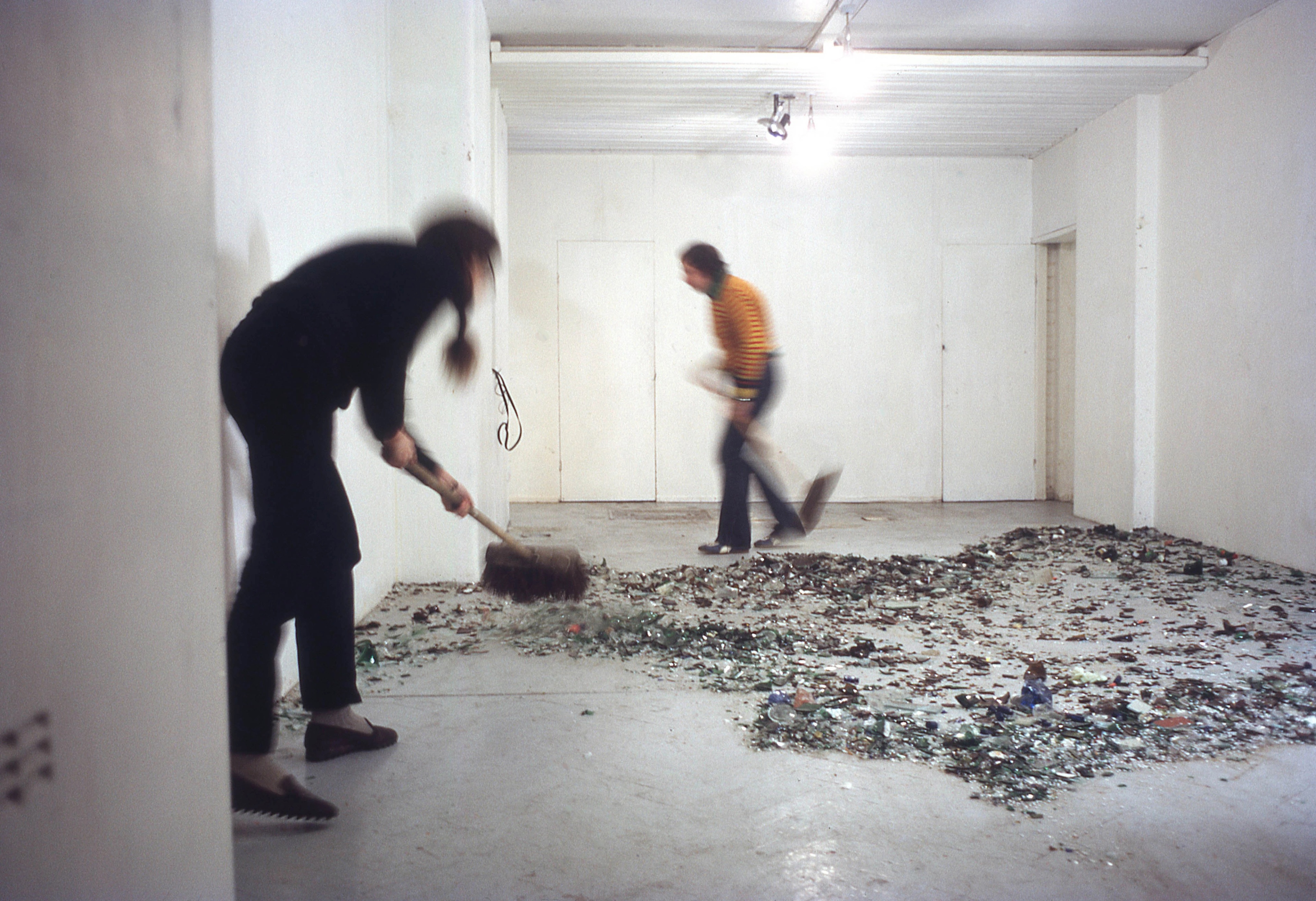 Two performers, Billy Apple and Annea Lockwood, sweeping broken glass around a white room. 