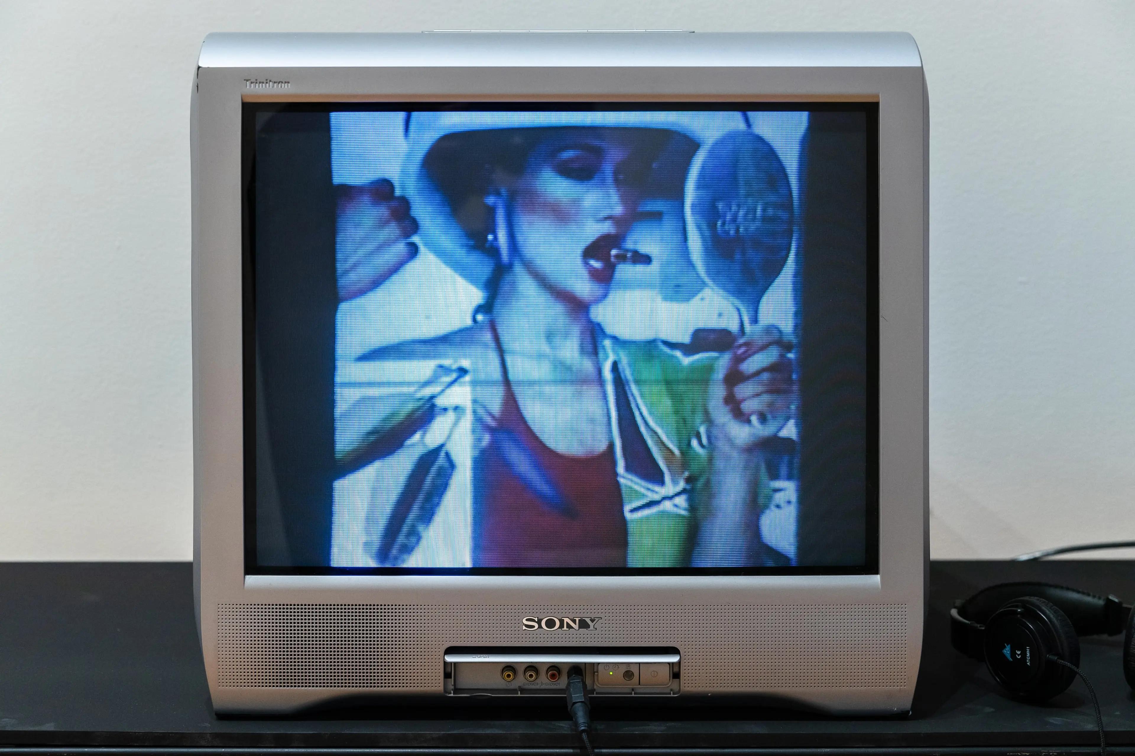 Small Sony television displaying video work of women, lipstick, feathers, looking into a mirror 