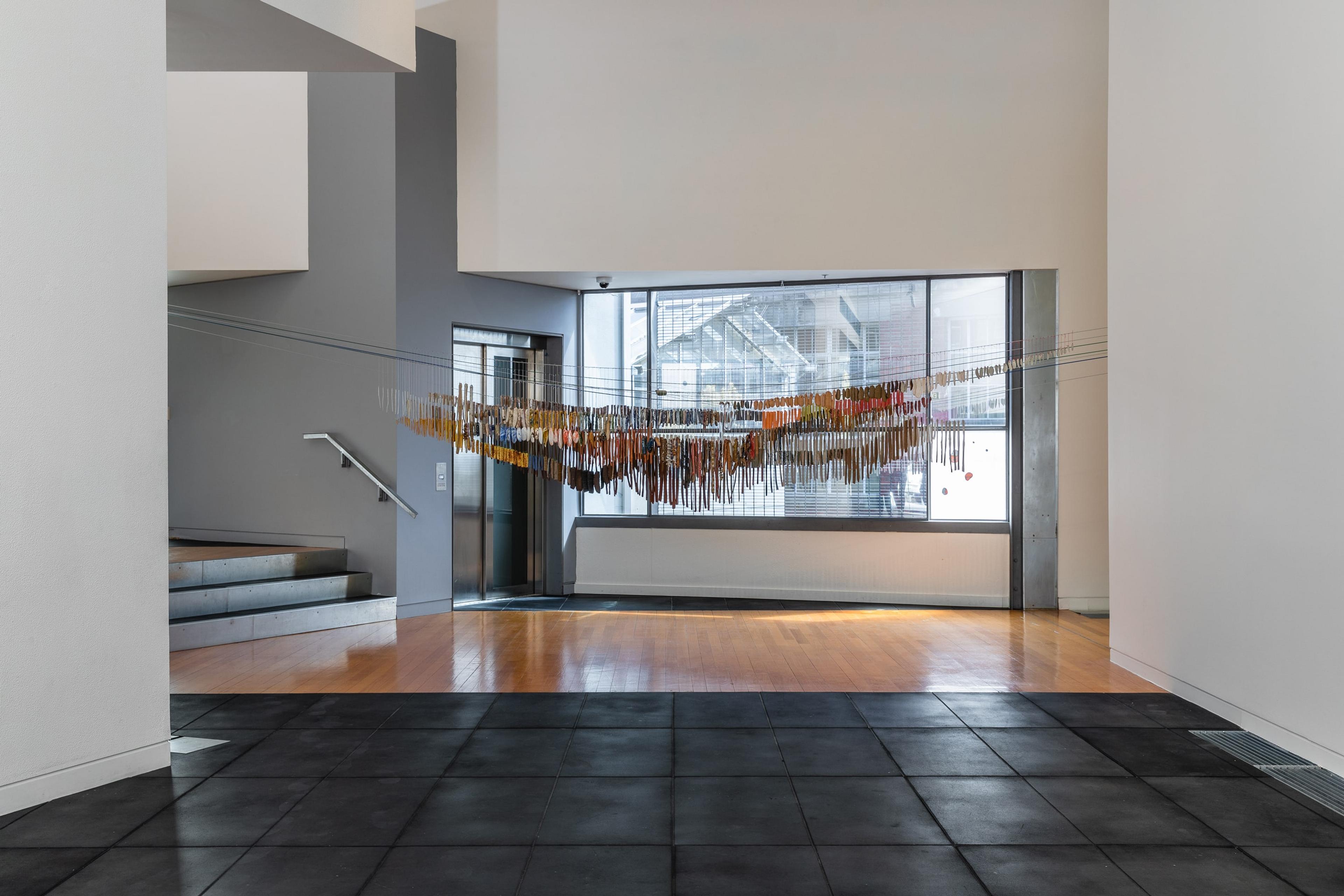 a wide view inside the Adam Art Gallery with a large installation of fine ceramic objects hanging infront of the window