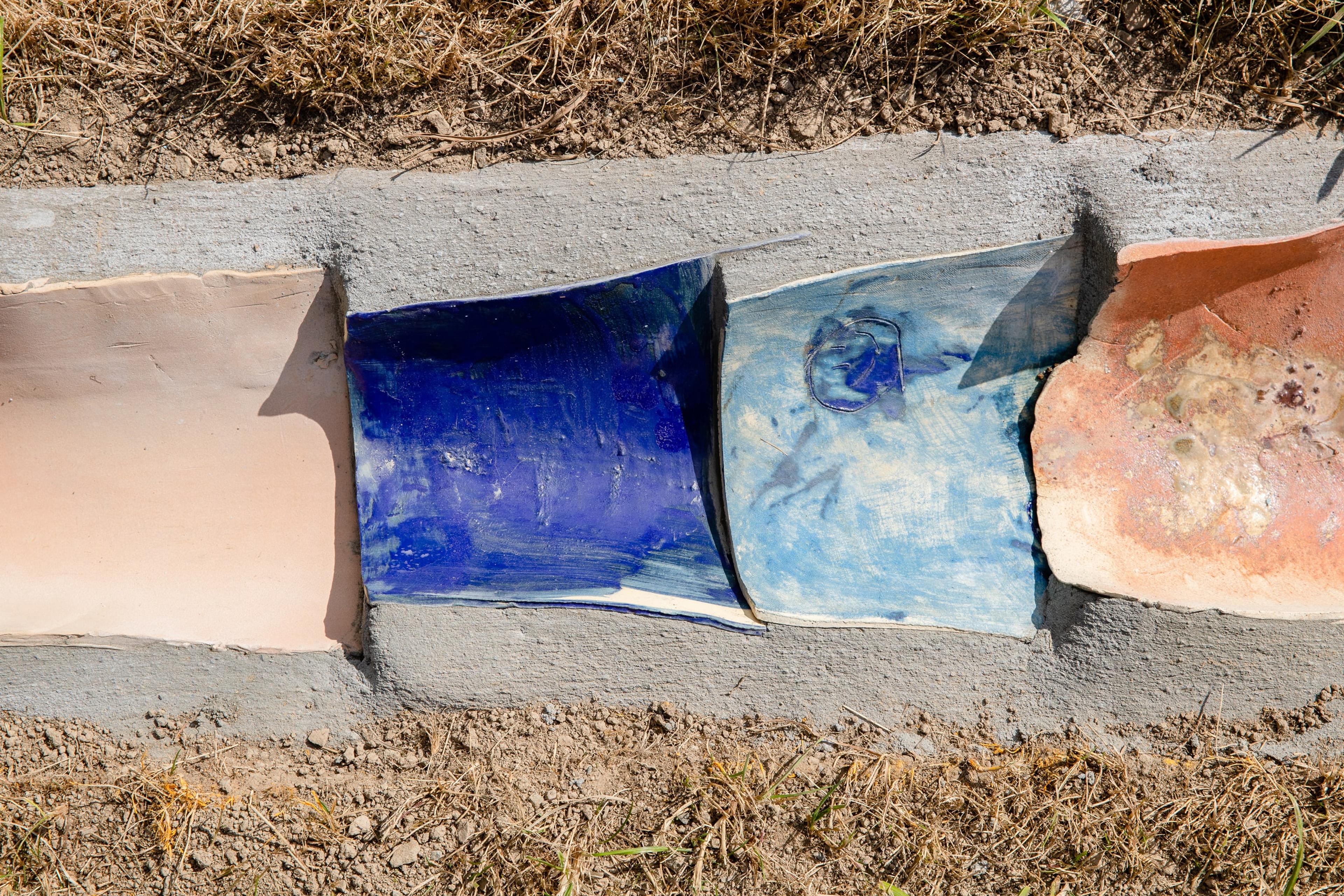 a drain gutter with dirt and grass on either side, set with rounded terracotta tiles of different colours