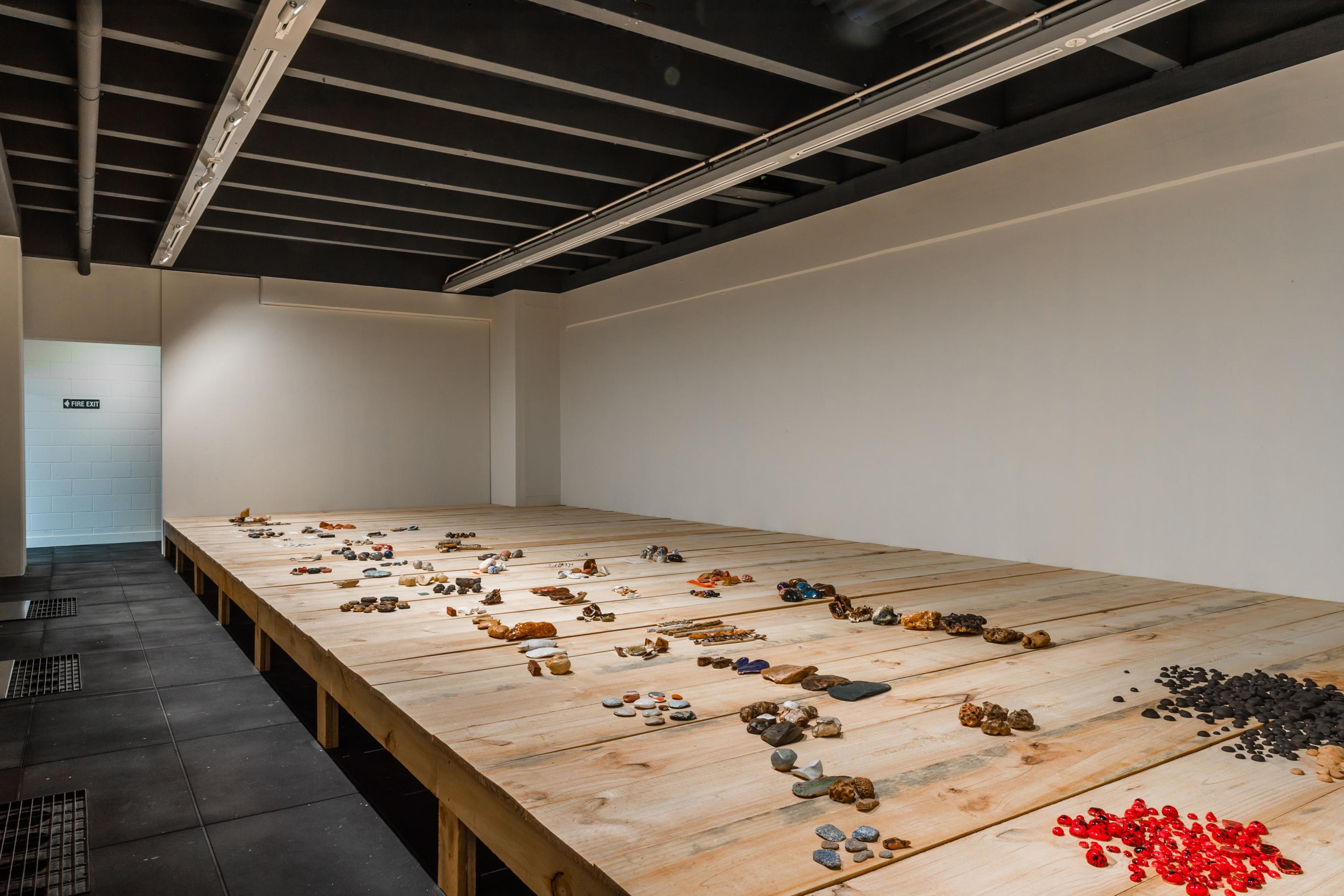 A wooden stage in a dimly lit white walled gallery, covered with groups of small objects
