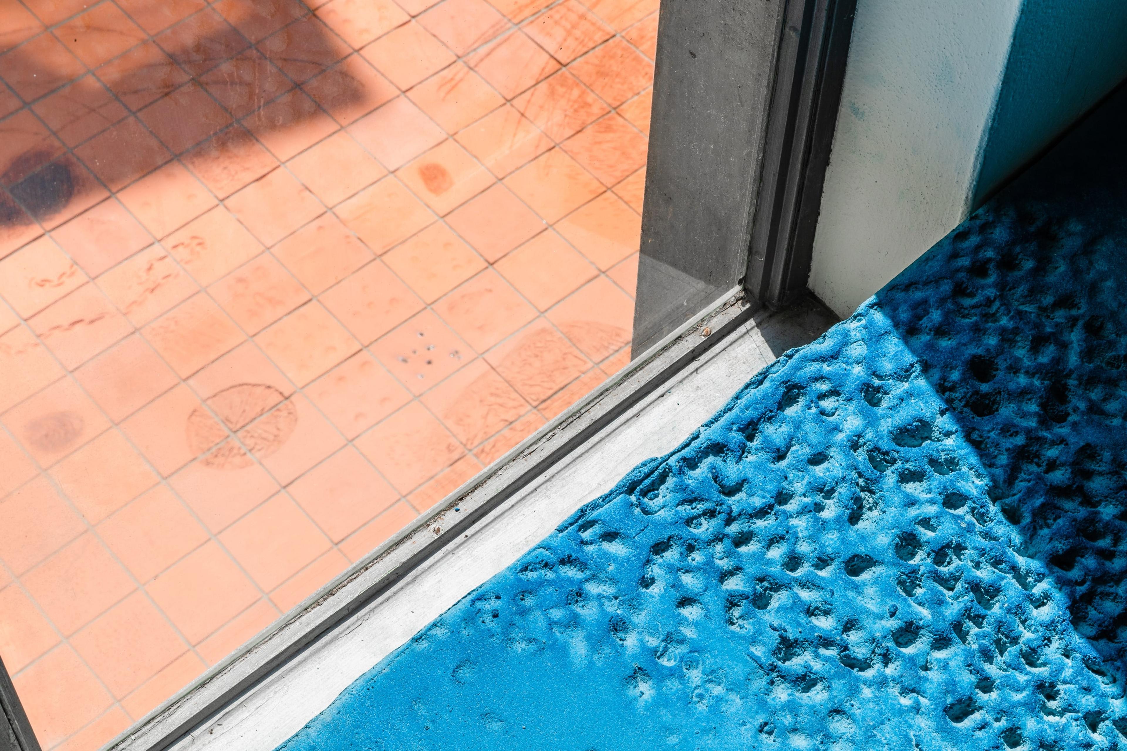 A view of the textured blue ground inside the gallery, and outside the window is textured terracotta tiles