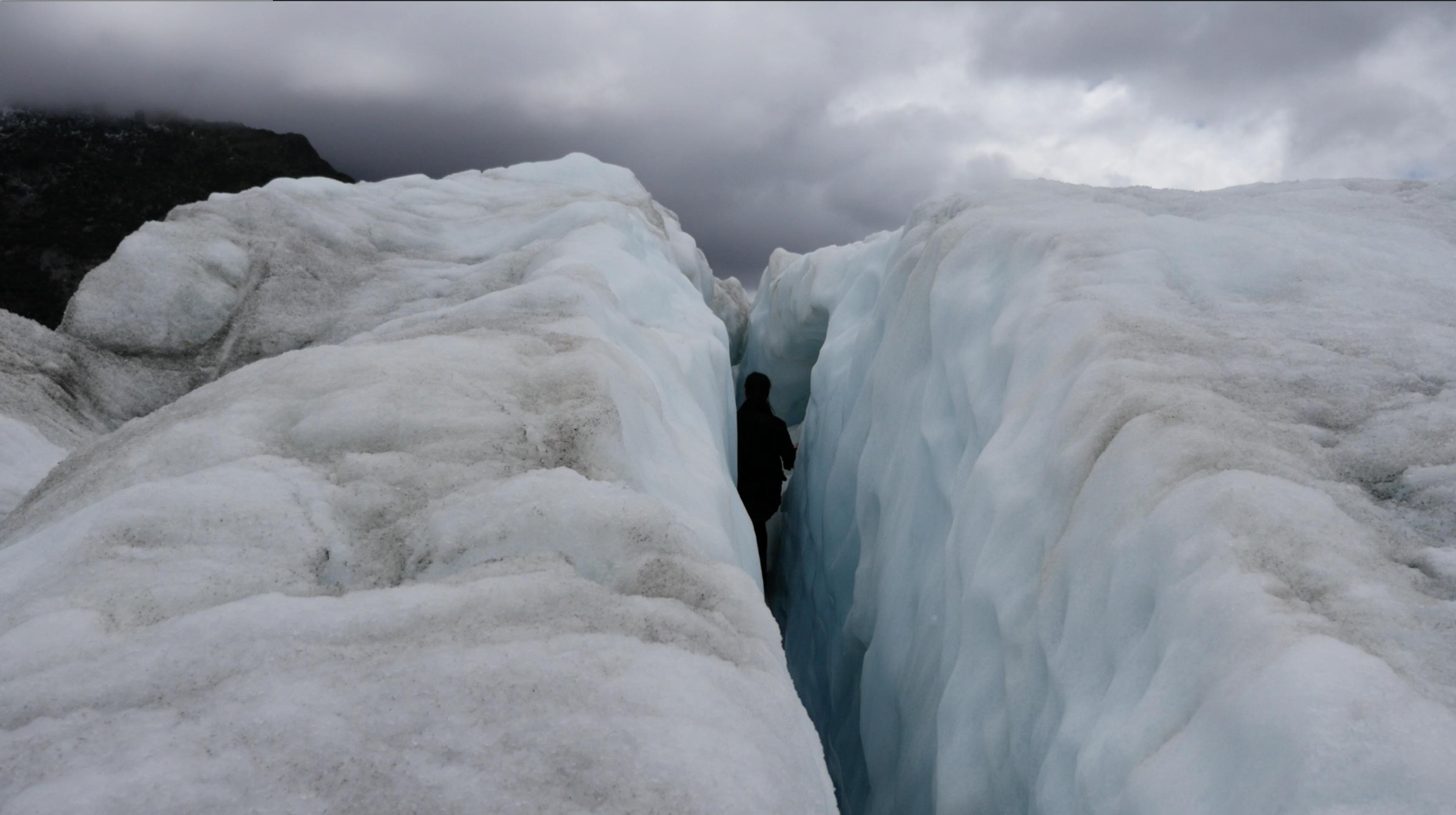 Video still, subject moving through glacier, grey stormy skies. 
