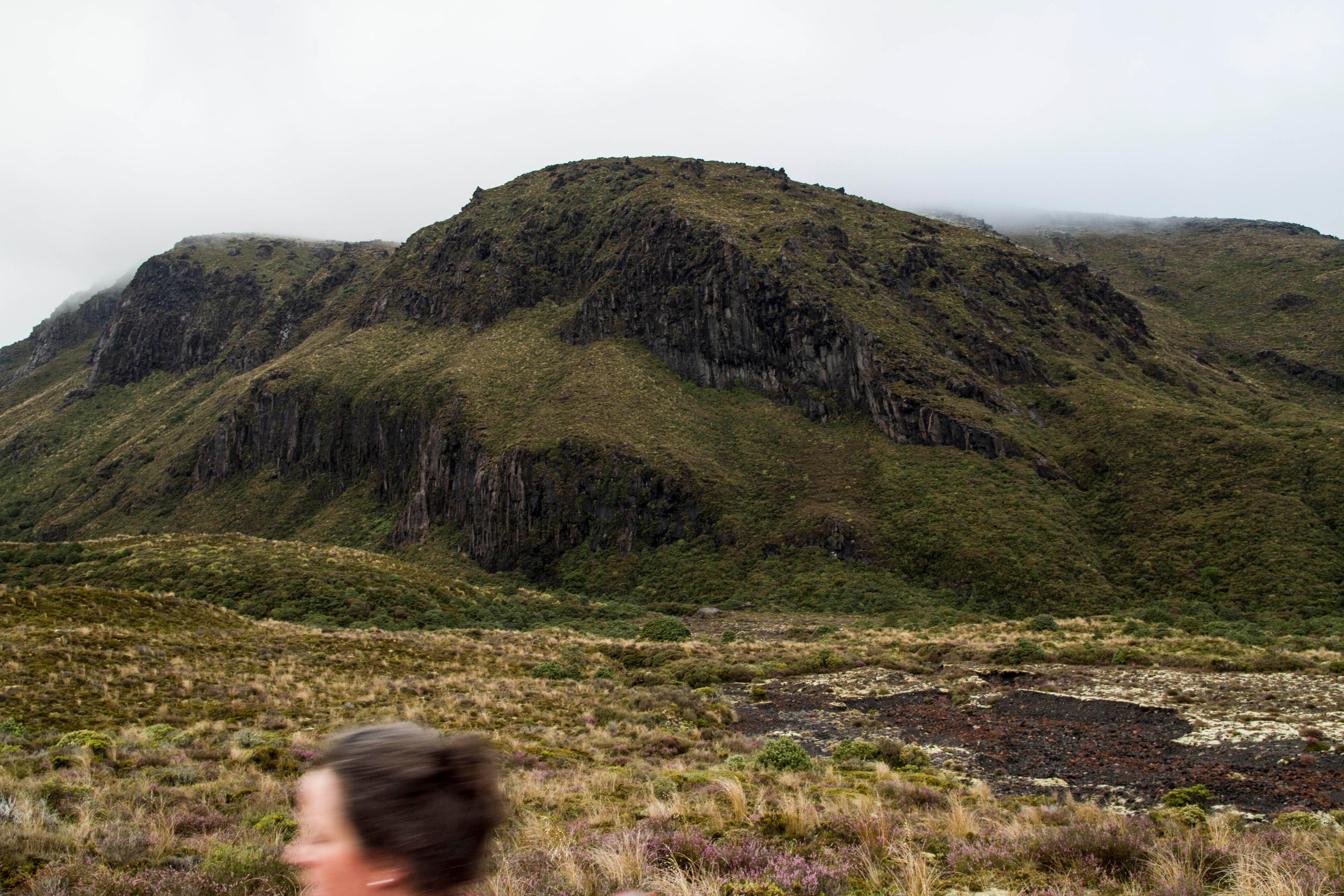 Women captured moving swiftly in the foreground of an image of a landscape on an overcast day.