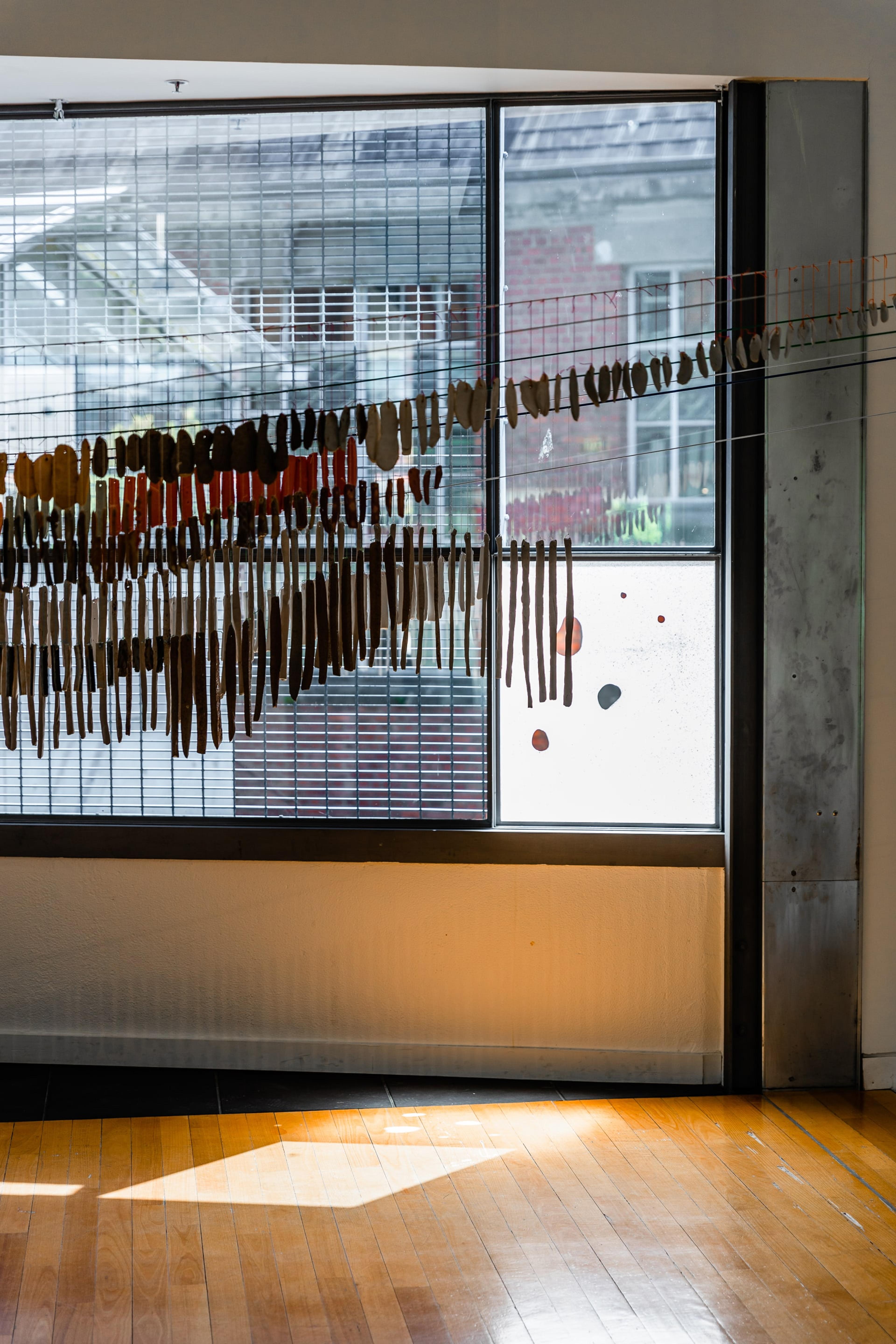 a view inside the Adam Art Gallery with a large installation of fine ceramic objects hanging in front of the window