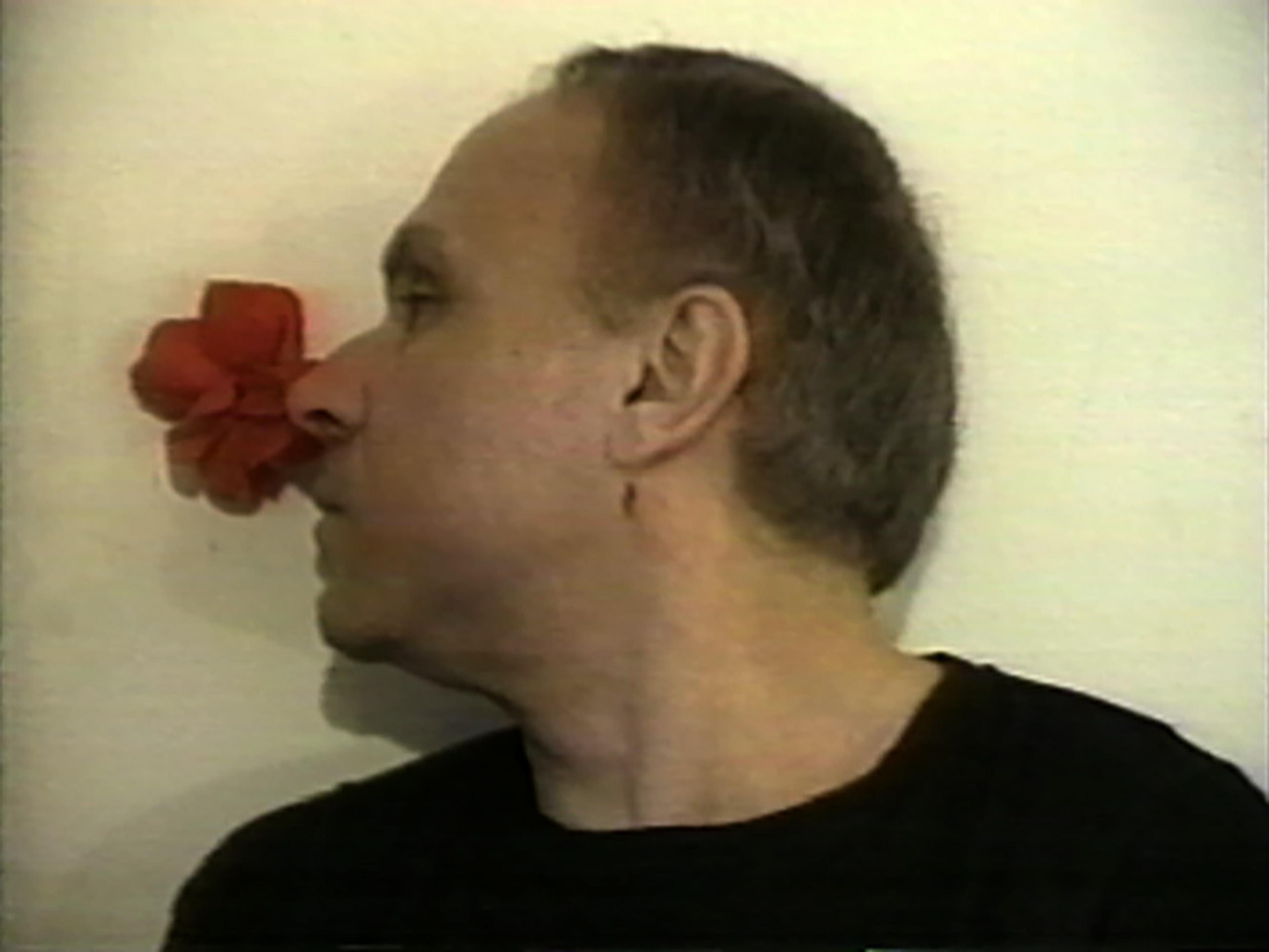 Video still showing Stuart Sherman smelling a rose over his right shoulder