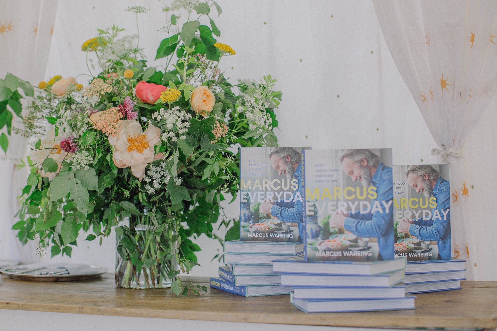 Three stacks of Marcus Everyday books next to a large vase of flowers