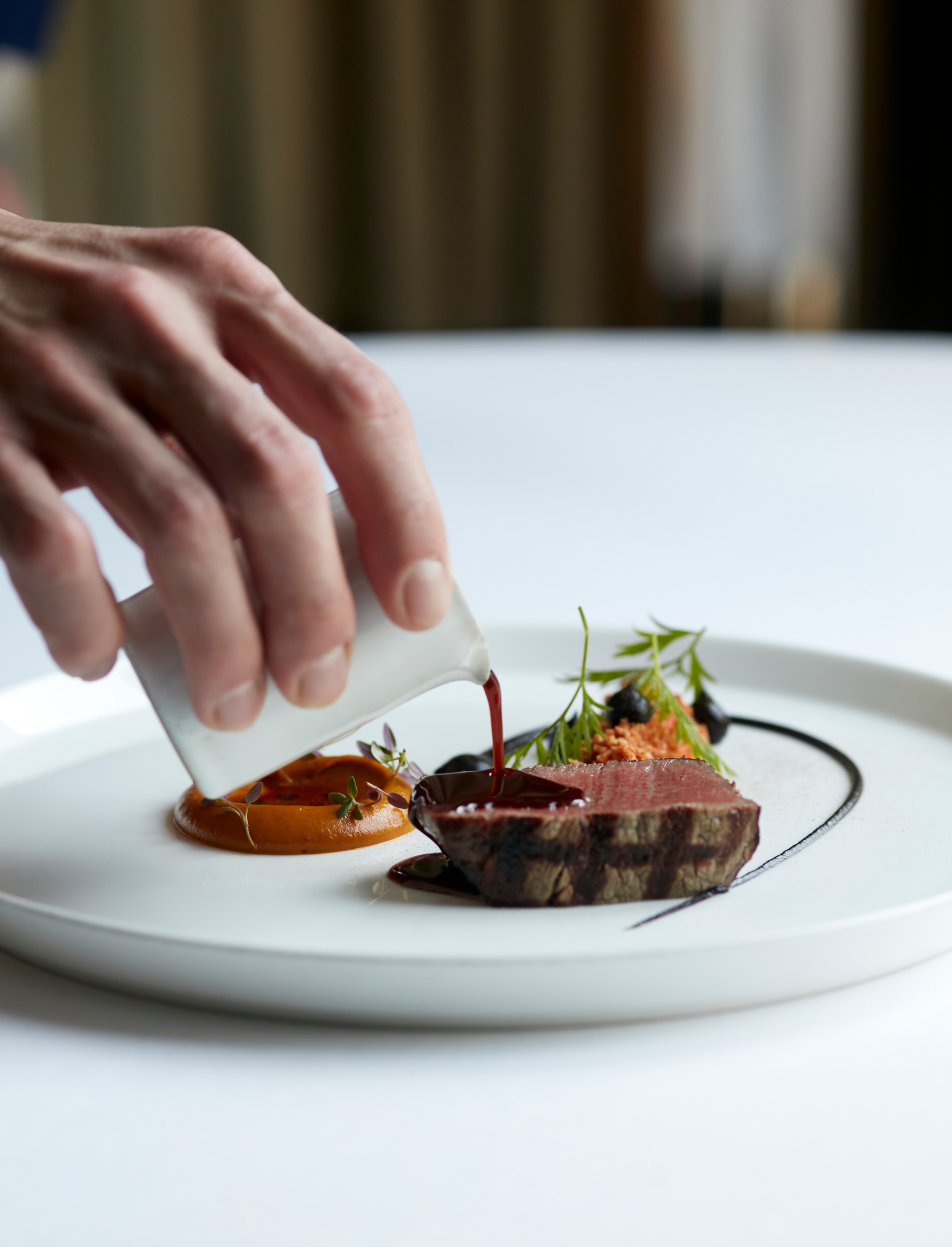 Sauce pouring over fillet of Galloway beef, served with carrot, pine nut and garlic 