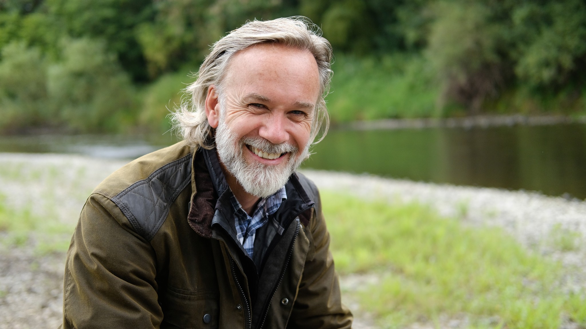 Marcus Wareing in front of a lake wearing an olive green jacket and blue checked shirt