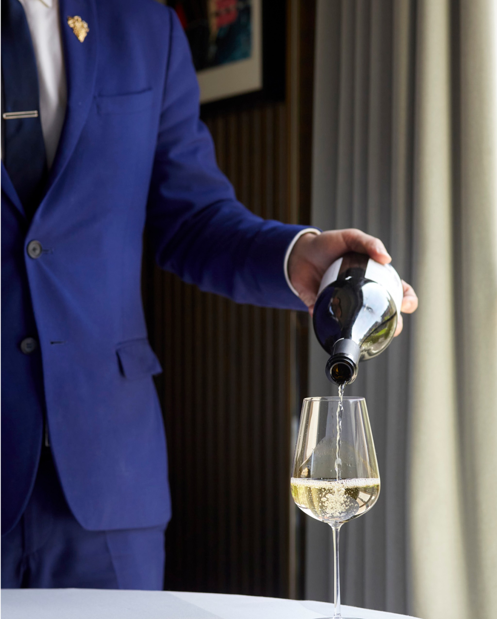 Man in a suit pouring white wine into a glass