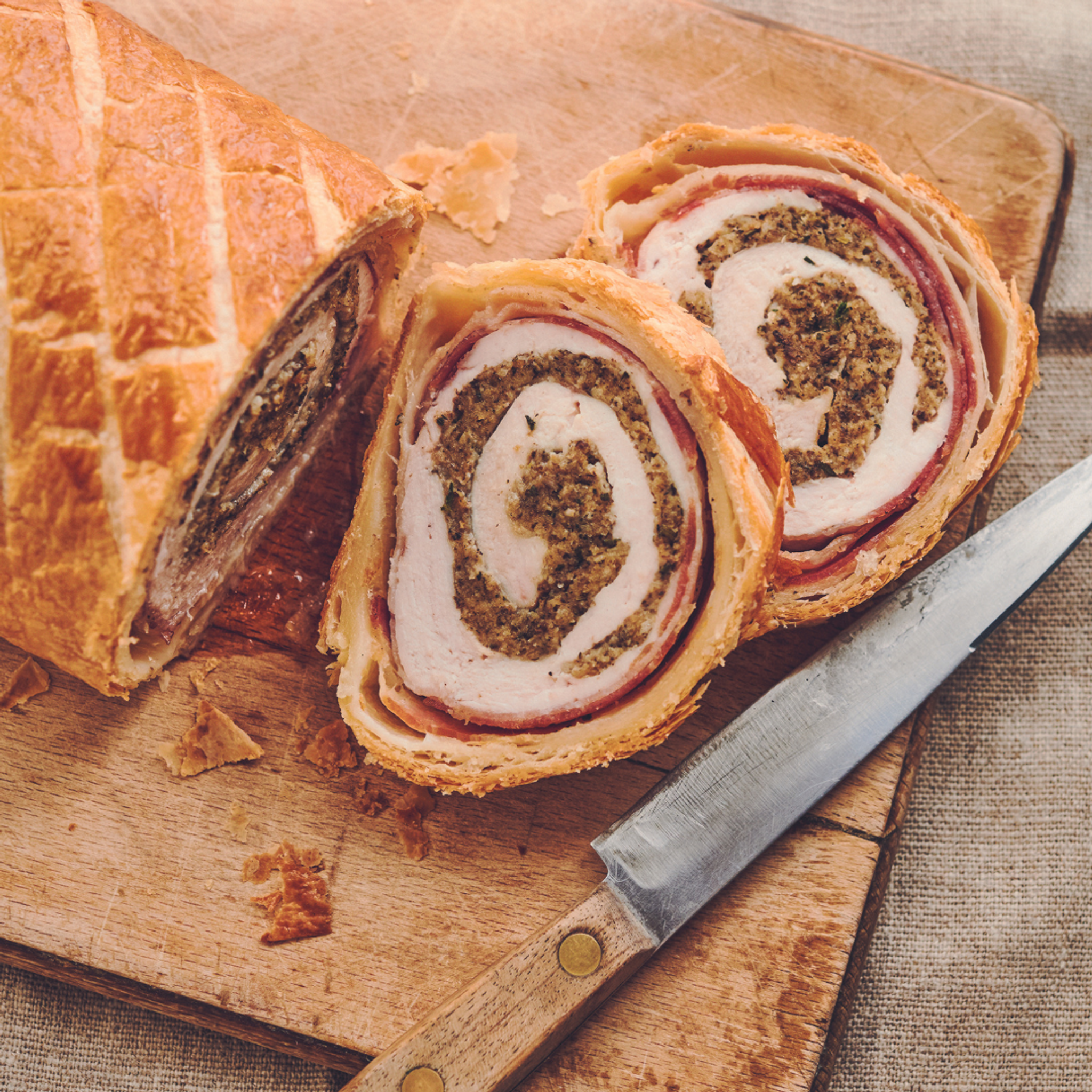 Chicken and mushroom wellington on wooden chopping board with knife
