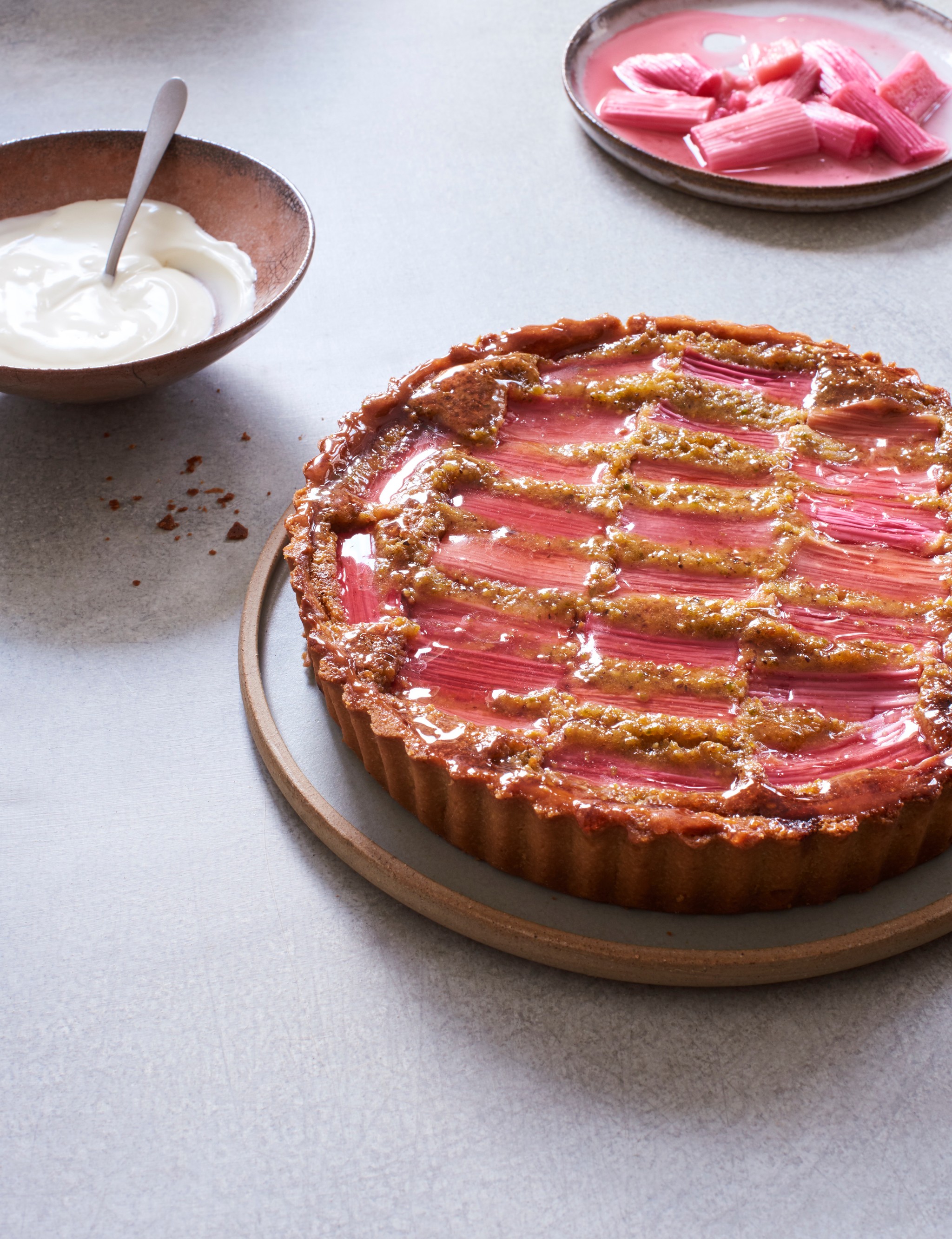 rhubarb and pistachio tart in foreground, with plate of rhubarb at the back