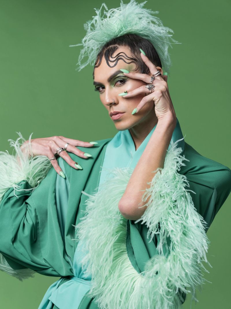 A closeup portrait of ShayShay in green robe and feathers