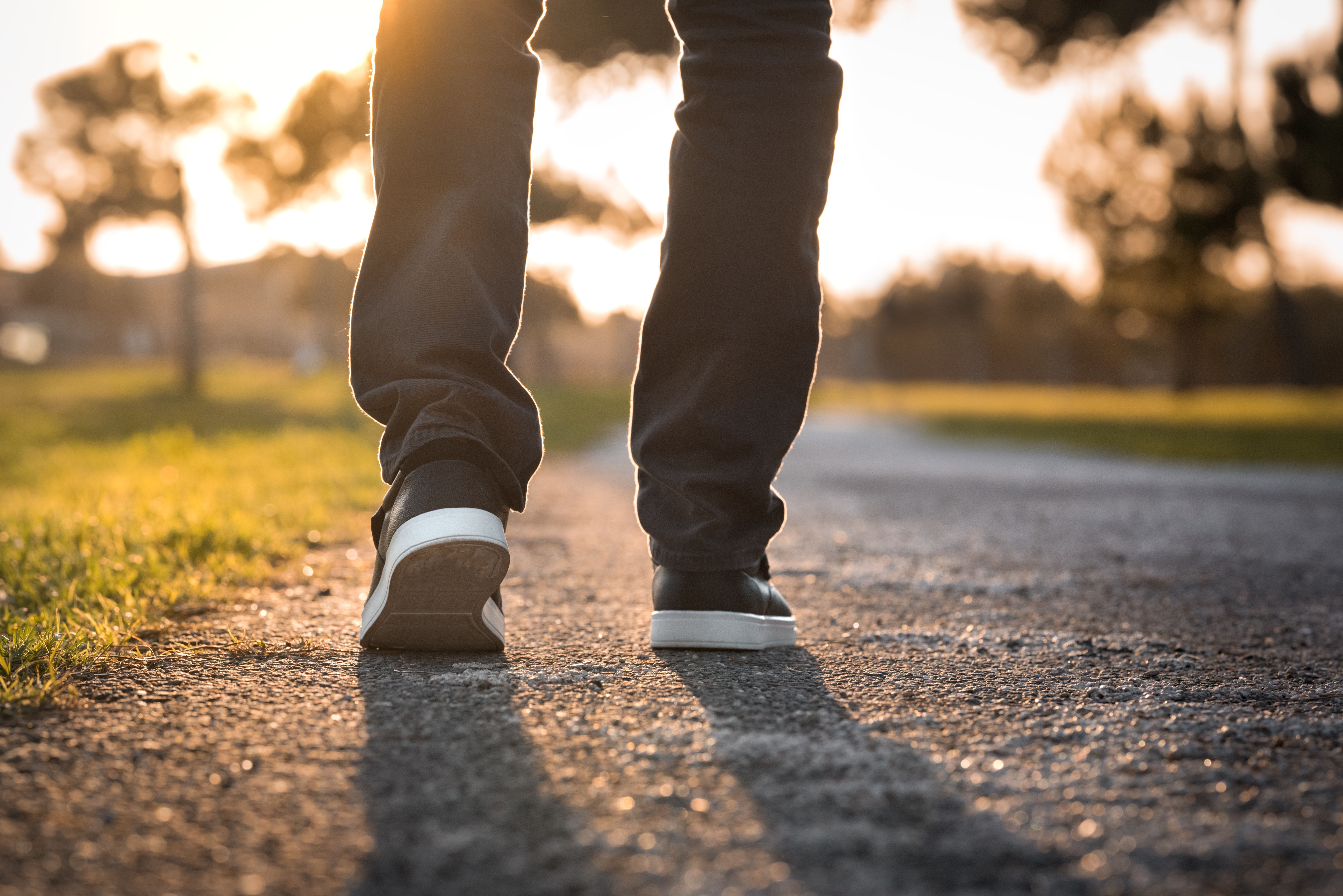 A person walking away along a tarmac path at sunset, seen from behind at knee height.