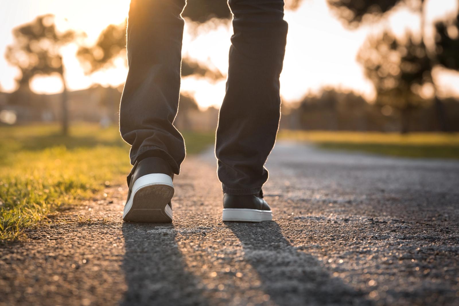A person walking away along a tarmac path at sunset, seen from behind at knee height.