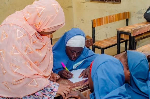 A facilitator supports a schoolgirl as she writes during a learning activity.