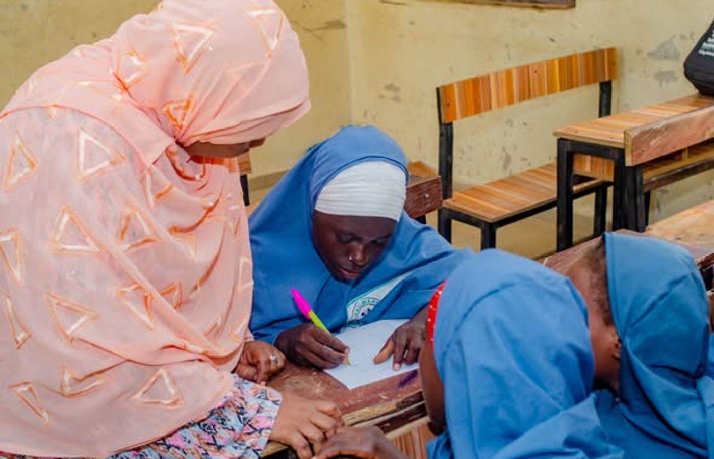 A facilitator supports a schoolgirl as she writes during a learning activity.
