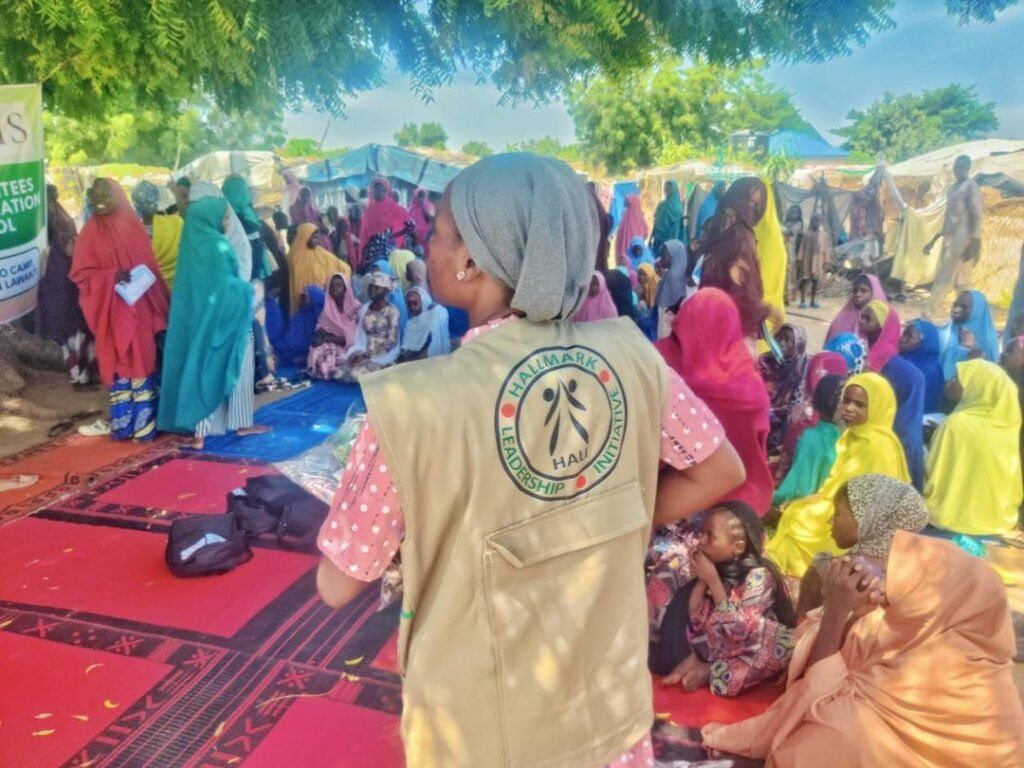 A HALI team member works alongside women and children during a community activity in Northeast Nigeria.