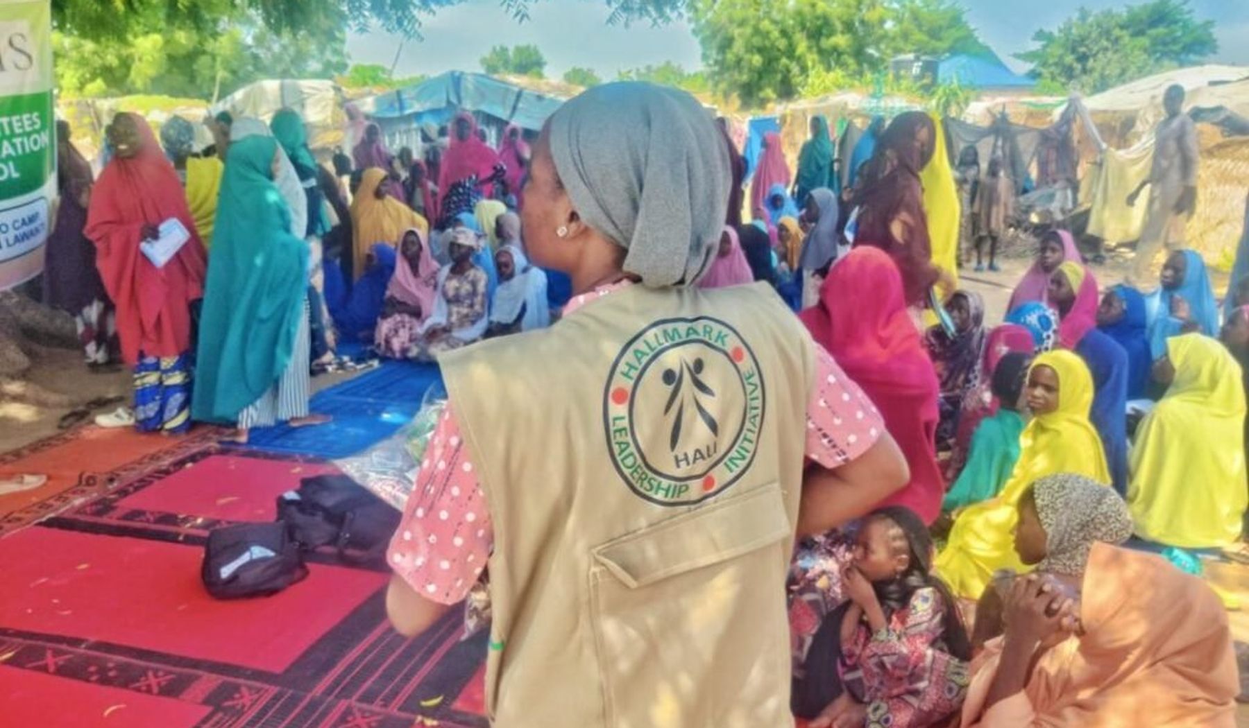 A HALI team member works alongside women and children during a community activity in Northeast Nigeria.