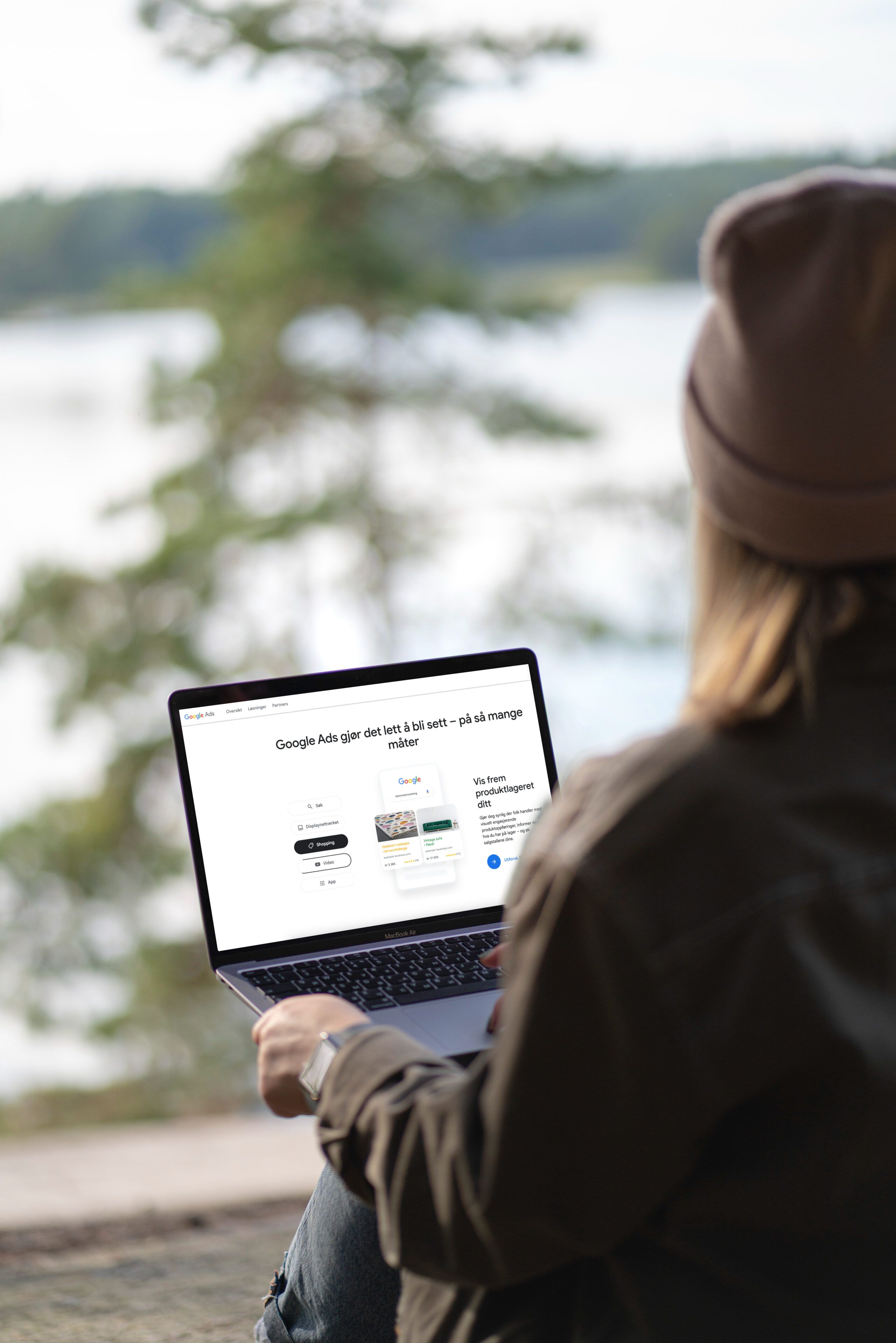 Person ved innsjø med laptop som viser Google Ads-nettside med norsk tekst om annonsering og produktkategorier.