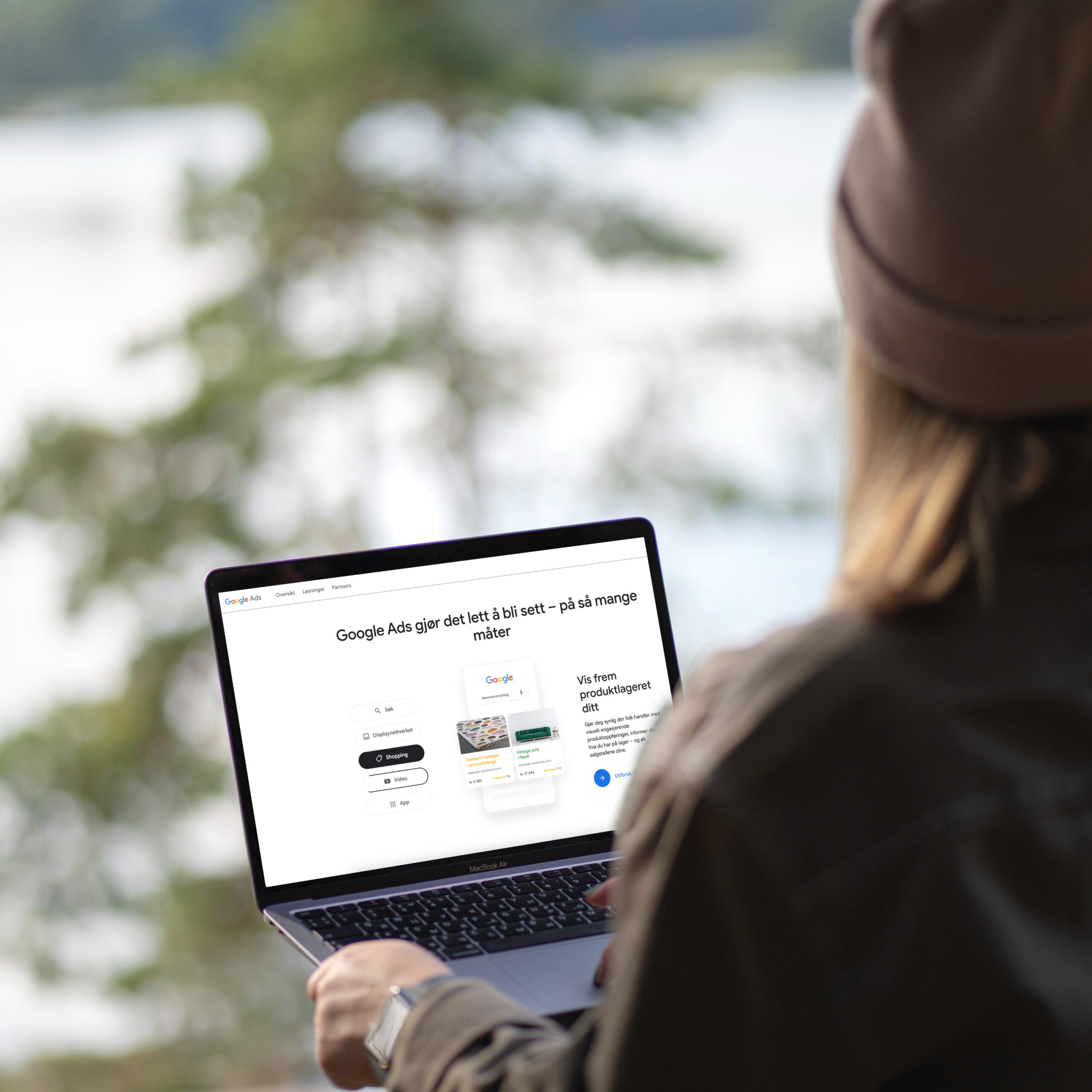 Person ved innsjø med laptop som viser Google Ads-nettside med norsk tekst om annonsering og produktkategorier.