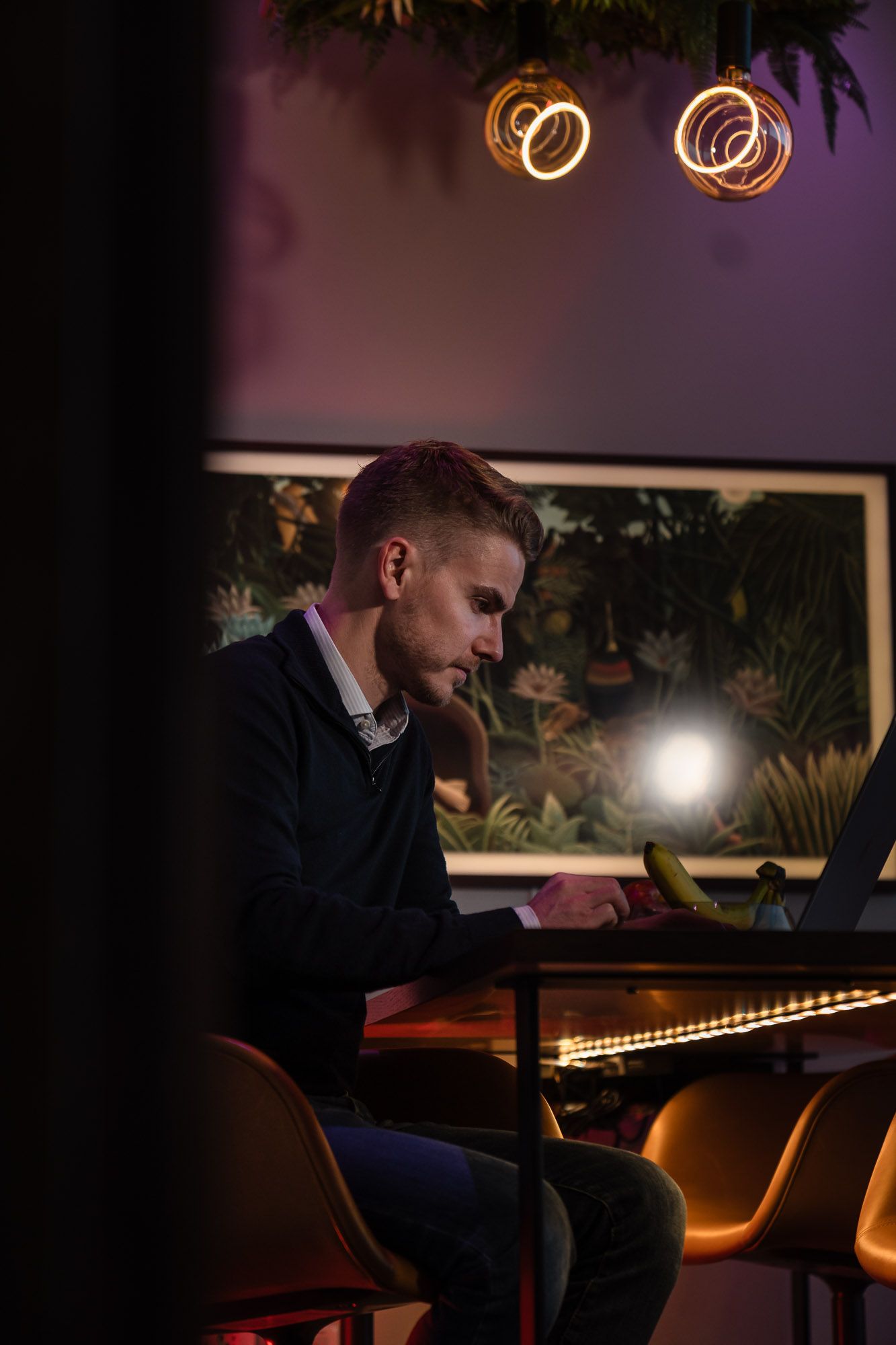 Mann ved laptop i moderne kontorinteriør med neon-sirkellamper og botanisk kunsttavle på vegg