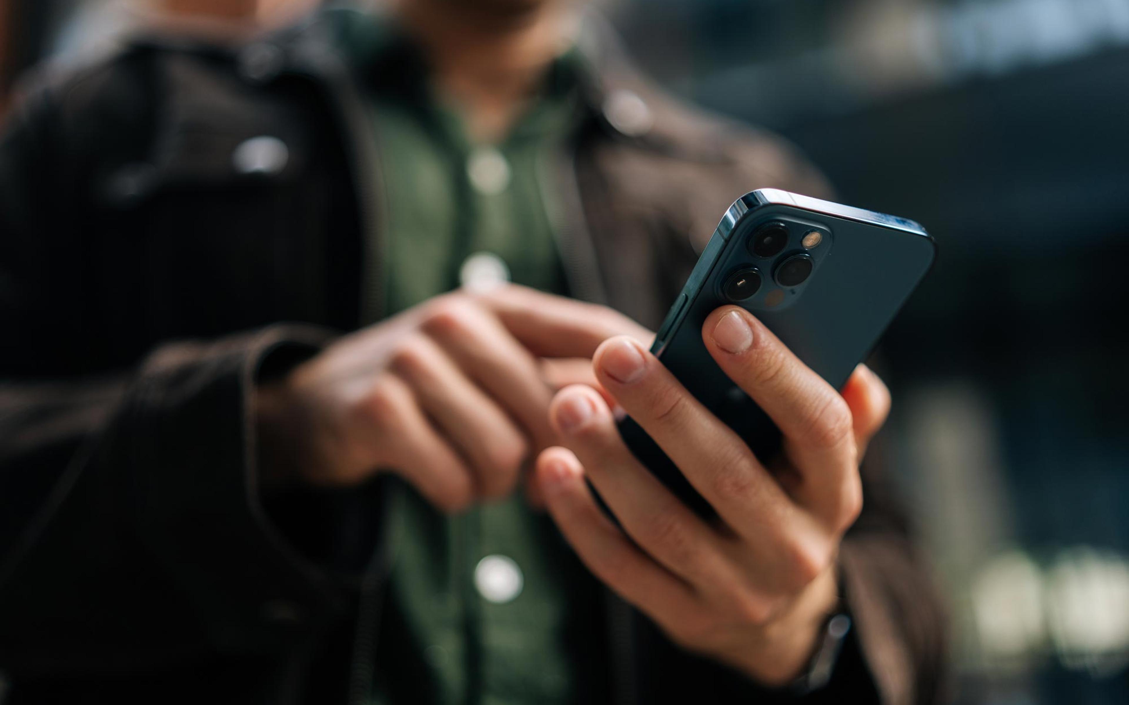 Person holder smarttelefon med trippelkamera og ser på skjermen, illustrerer mobil sosialmediebruk
