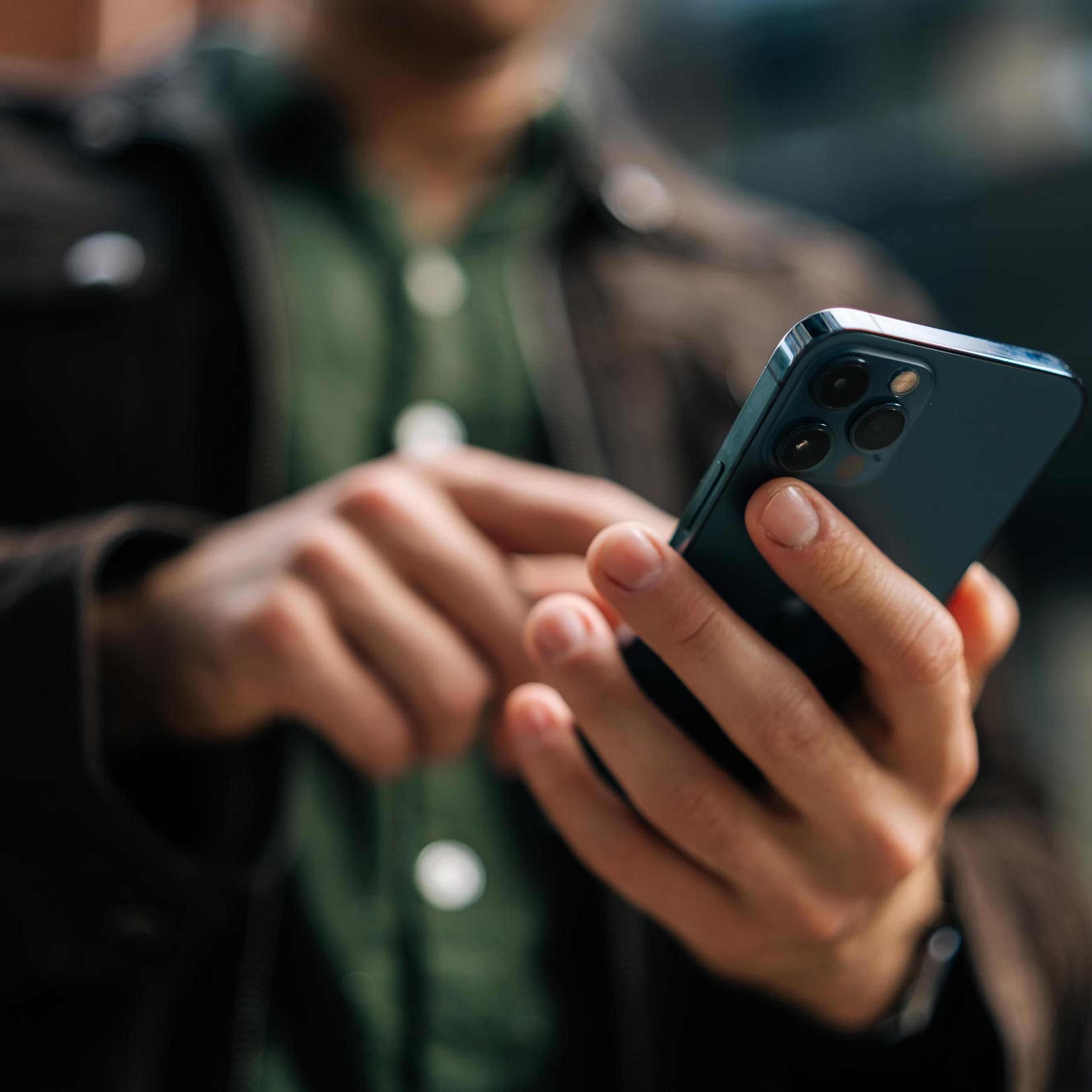 Person holder smarttelefon med trippelkamera og ser på skjermen, illustrerer mobil sosialmediebruk