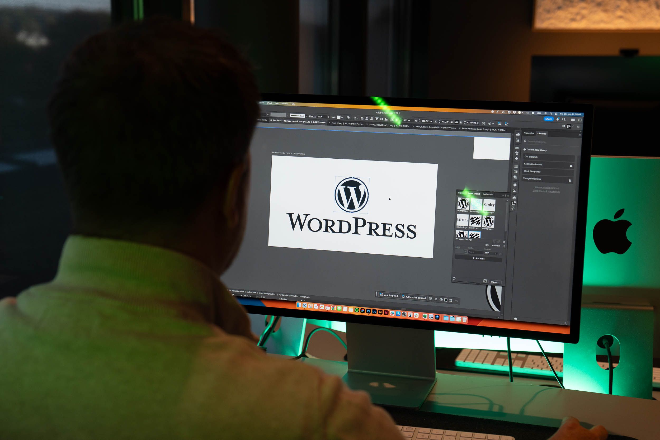 Designer arbeider i Adobe Creative Suite med WordPress-logo åpen på skjermen ved siden av Mac-enhet.