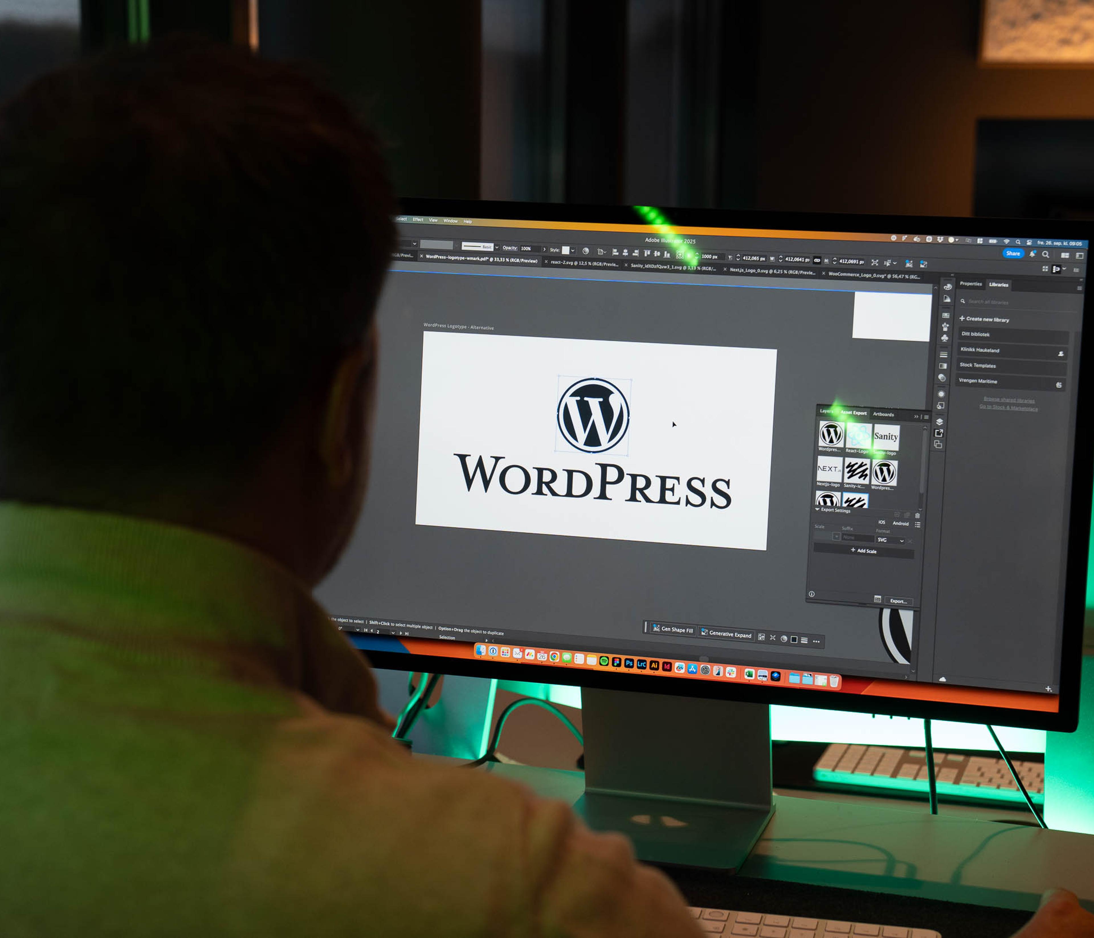 Designer arbeider i Adobe Creative Suite med WordPress-logo åpen på skjermen ved siden av Mac-enhet.