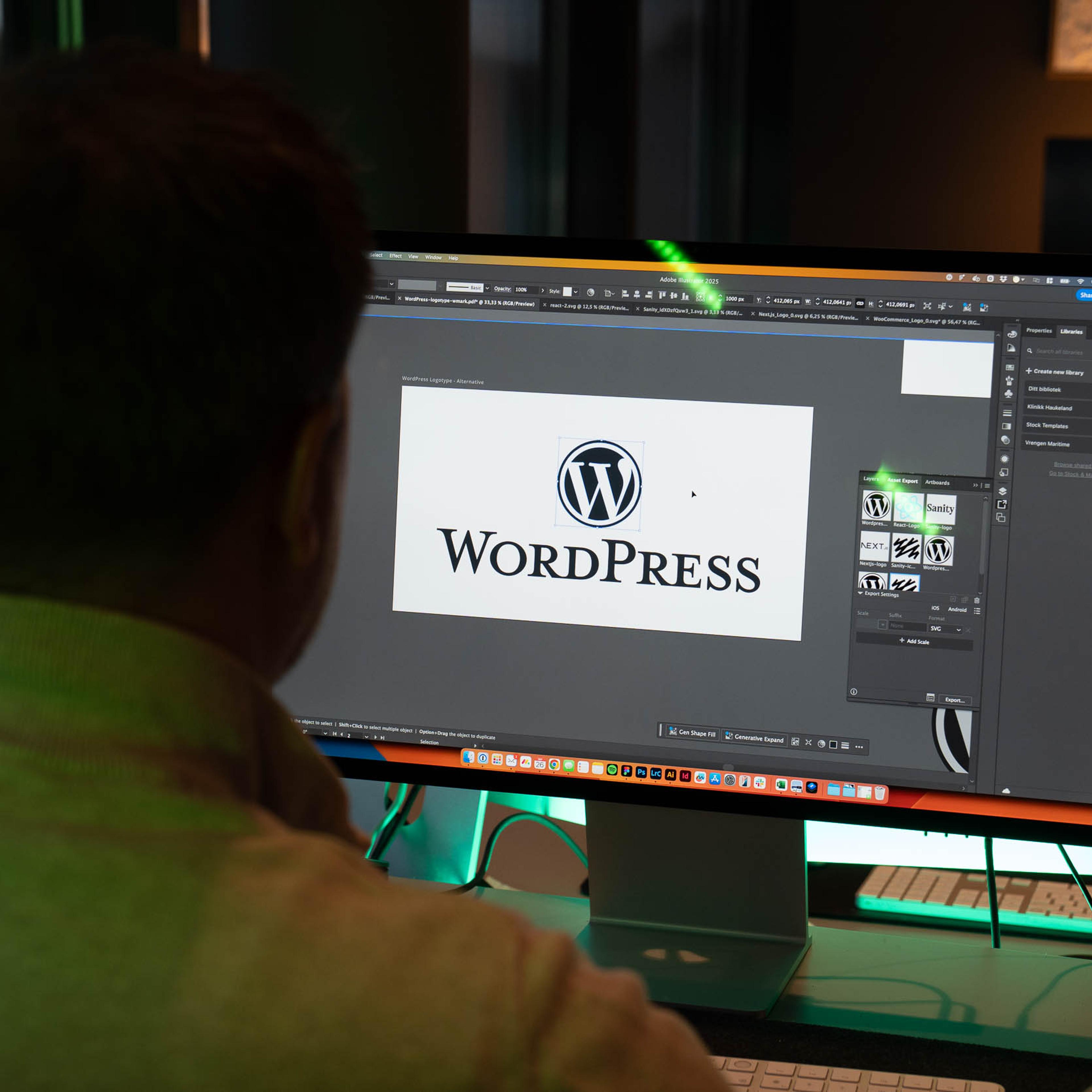 Designer arbeider i Adobe Creative Suite med WordPress-logo åpen på skjermen ved siden av Mac-enhet.