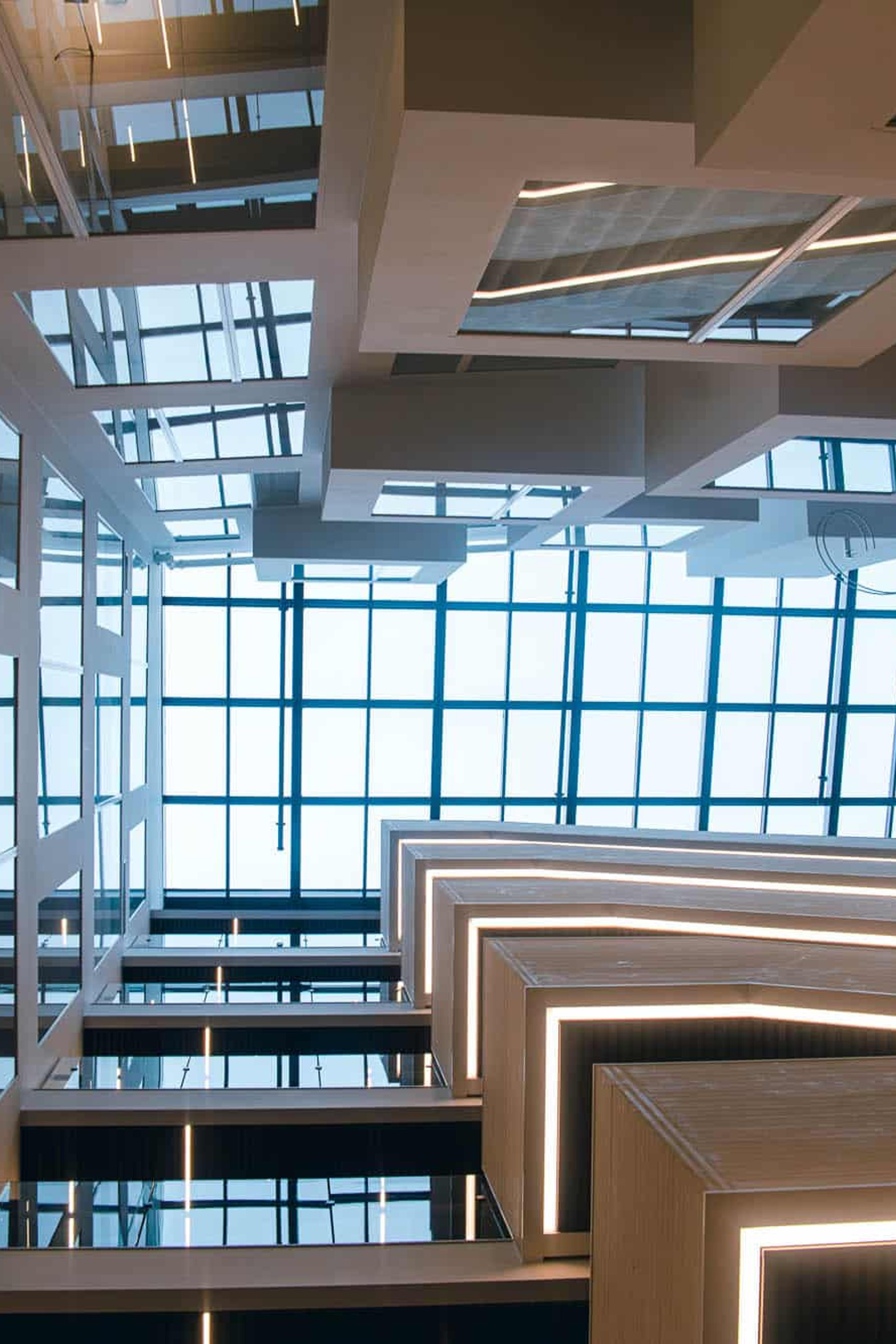 Moderne kontorlokale med store vinduer, betongsøyler og innebygd belysning i tak og trapperekkverk.