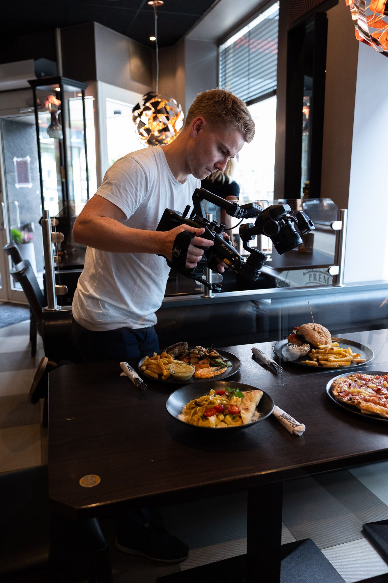 Videograf fotograferer matrett med professionelt kamera i moderne restaurant med svart bord og stilfull belysning.