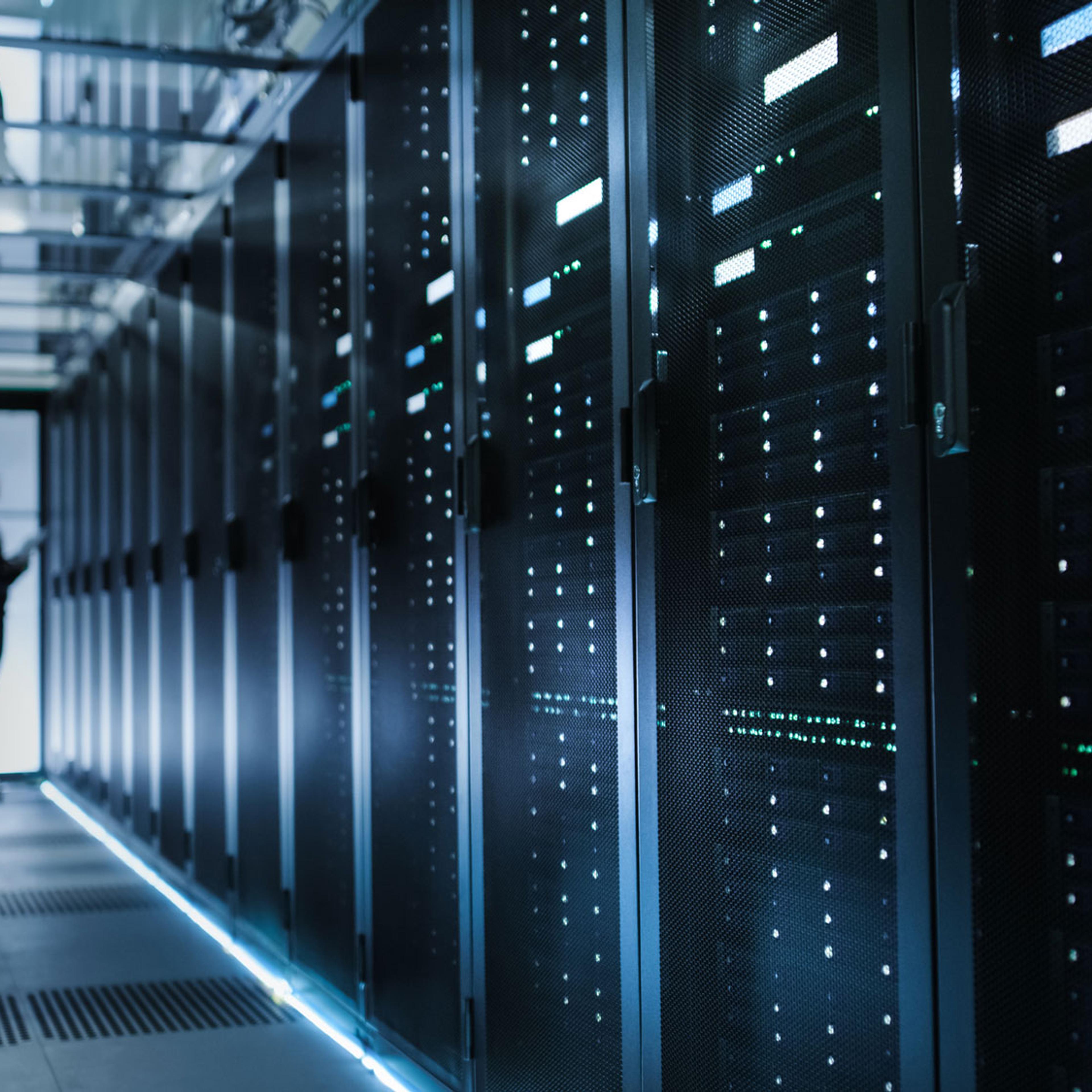 Tekniker inspiserer serverutstyr i en moderne serverhall med belyst gulv og lysende indikatorer på serverrack.