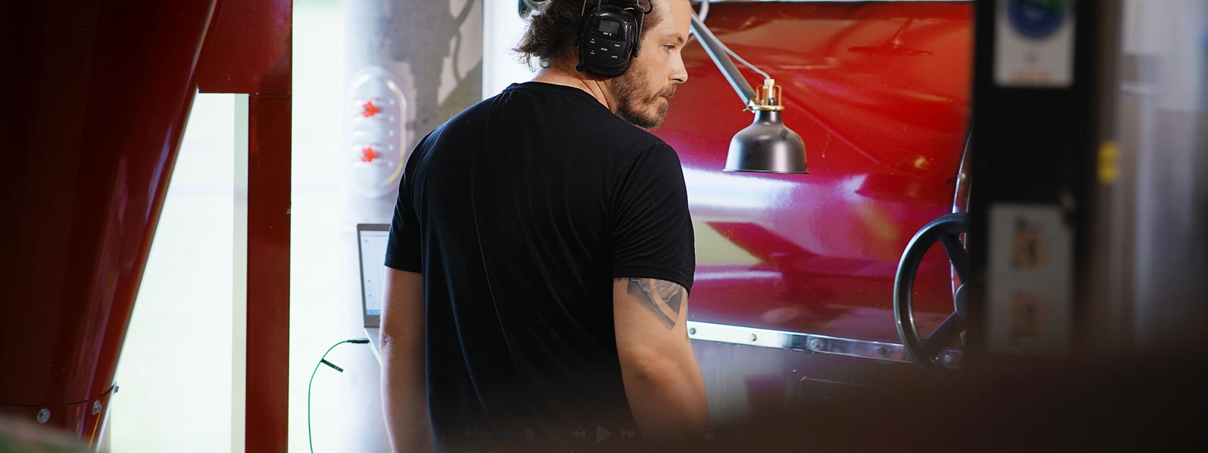 Mann med hodetelefoner og mikrofon i podcast- eller radiostudio med rødt lys og utstyr i bakgrunnen.