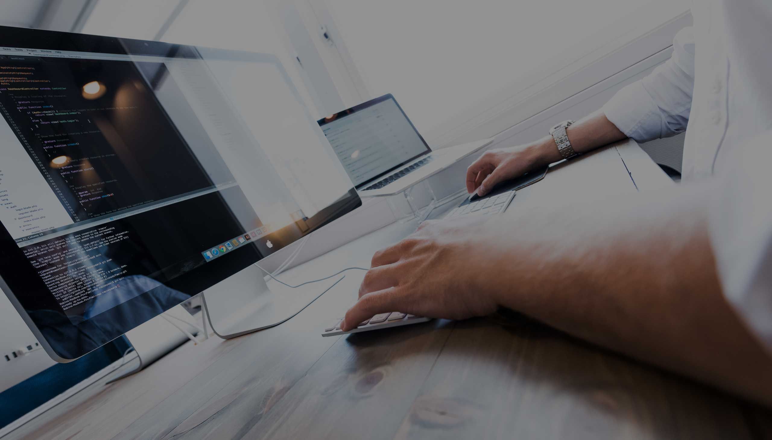 Person arbeider ved datamaskiner med kode på skjermen, illustrerer digital utvikling og IT-arbeid på kontor.