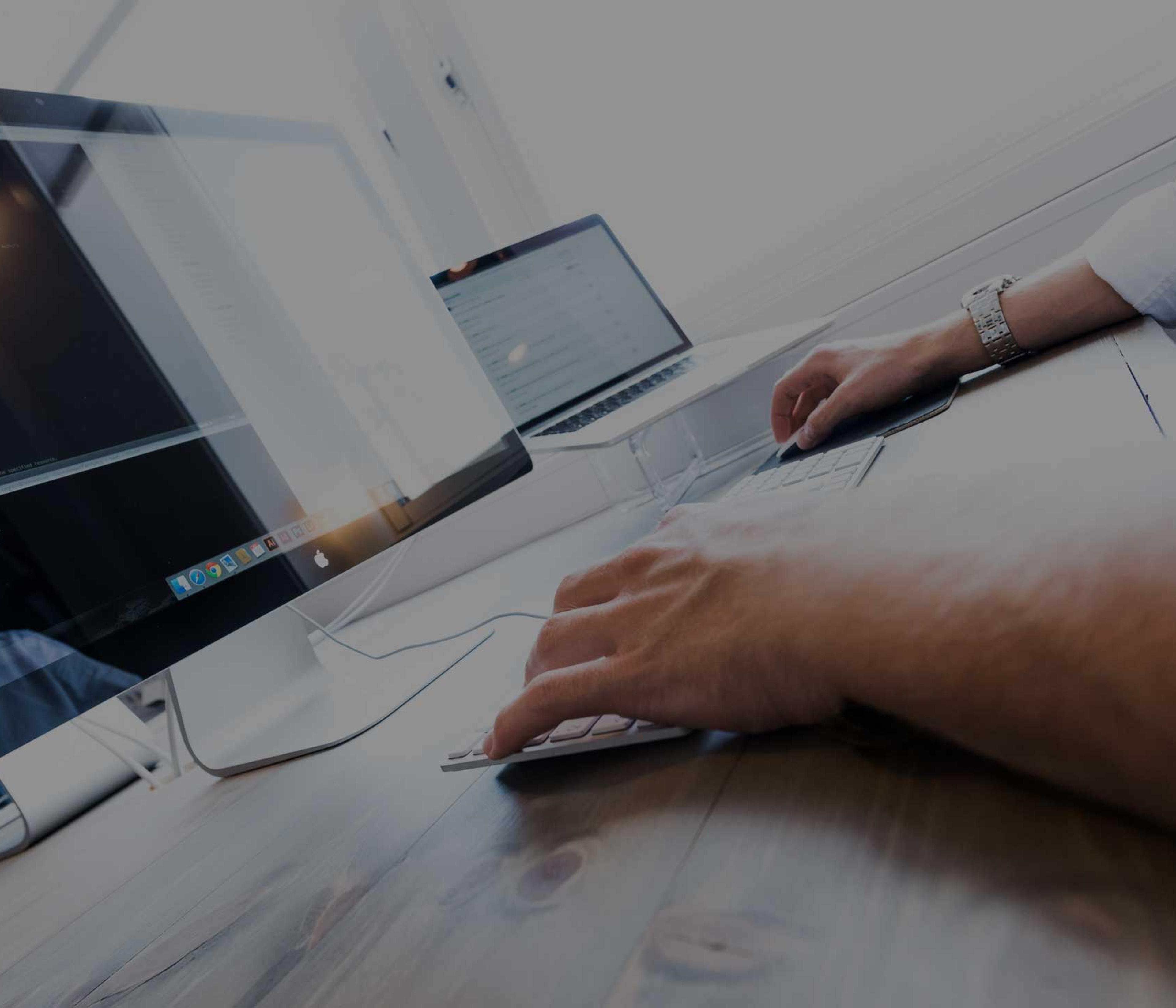 Person arbeider ved datamaskiner med kode på skjermen, illustrerer digital utvikling og IT-arbeid på kontor.
