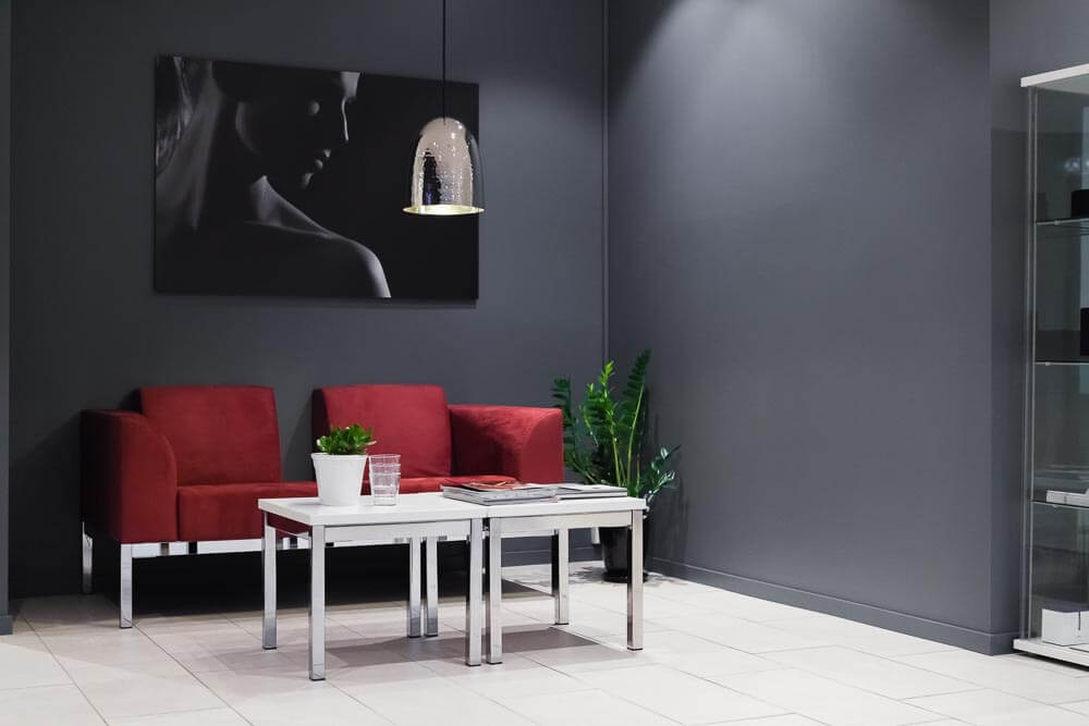 Moderne venteværelse med grå vegger, rød sofa, hvite møbler og kunstnerisk sort veggdekorasjon med pendant-lampe.