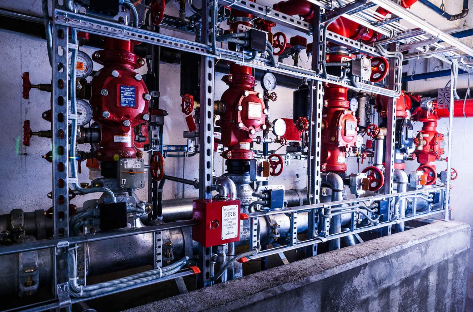Industriell brannslokking-system med røde ventiler, pumper og blå rør montert på stålramme.