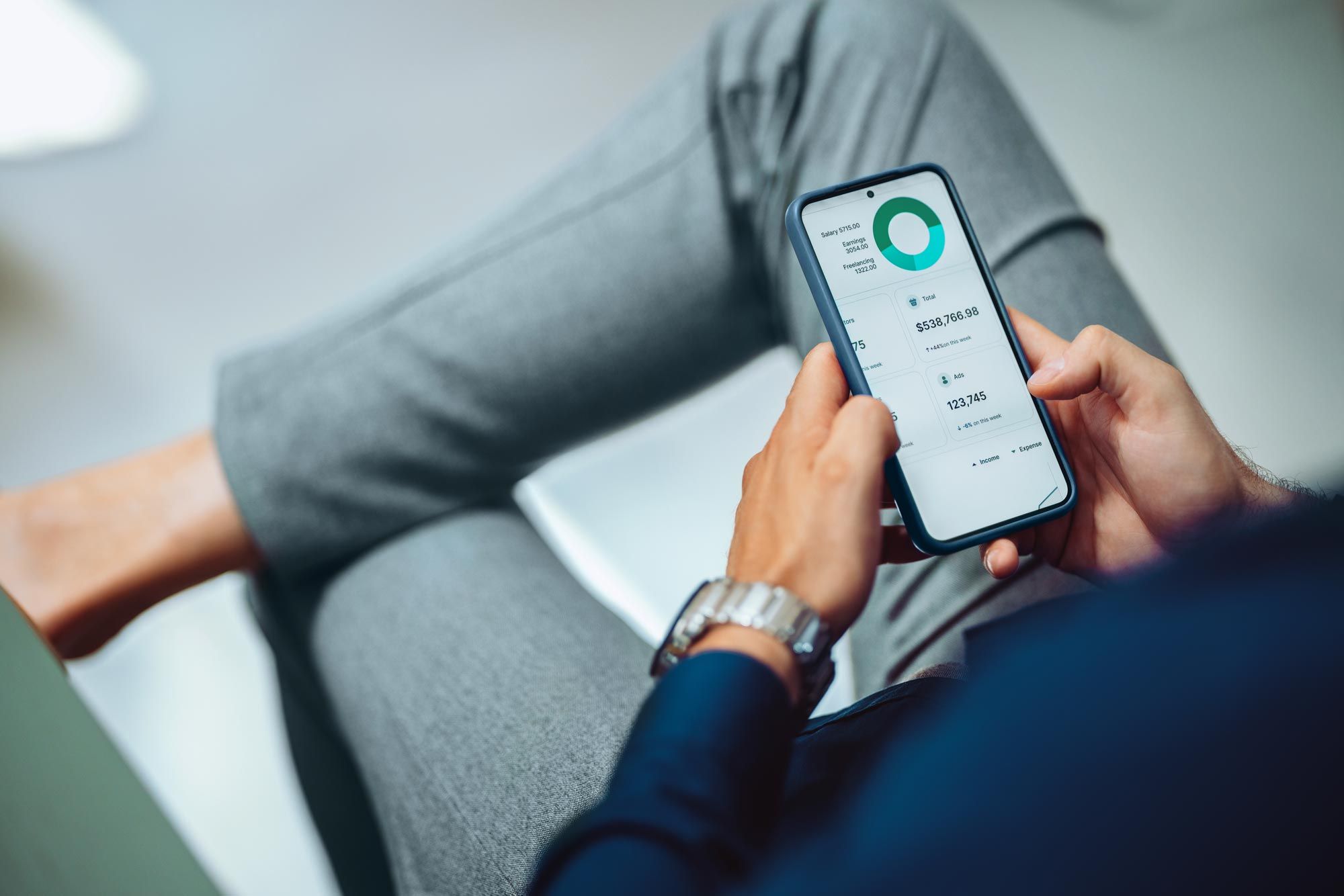 Person holder smarttelefon med finansiell dashboardapp som viser sparesamtale, utgifter og økonomisk oversikt.