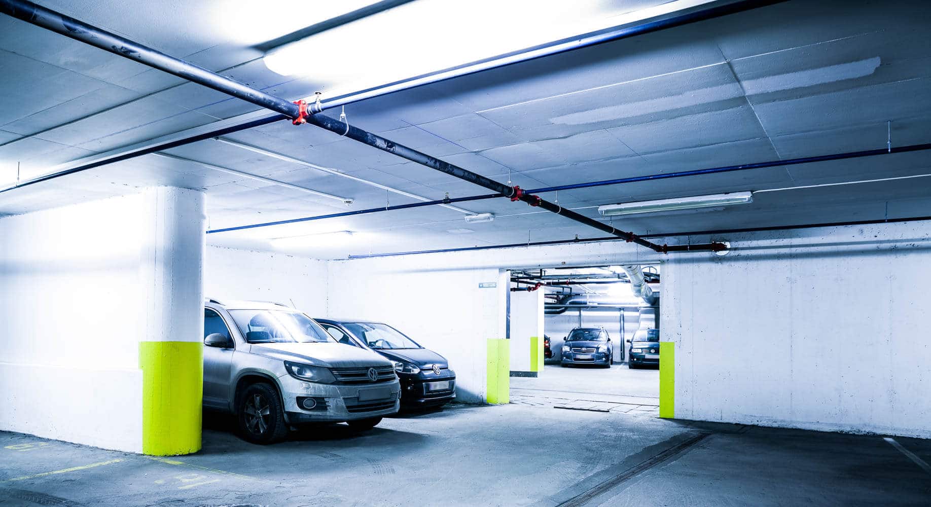 Undersjøss parkeringshus med hvite biler parkert ved neon grønne søyler og lysarmatur i taket.
