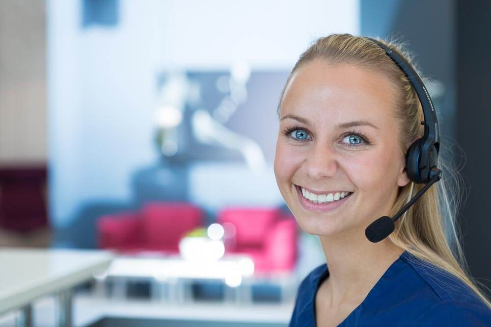 Smilende kvinne med headset i profesjonelt kontormiljø, tilsynelatende kundeservicemedarbeider eller support-agent.