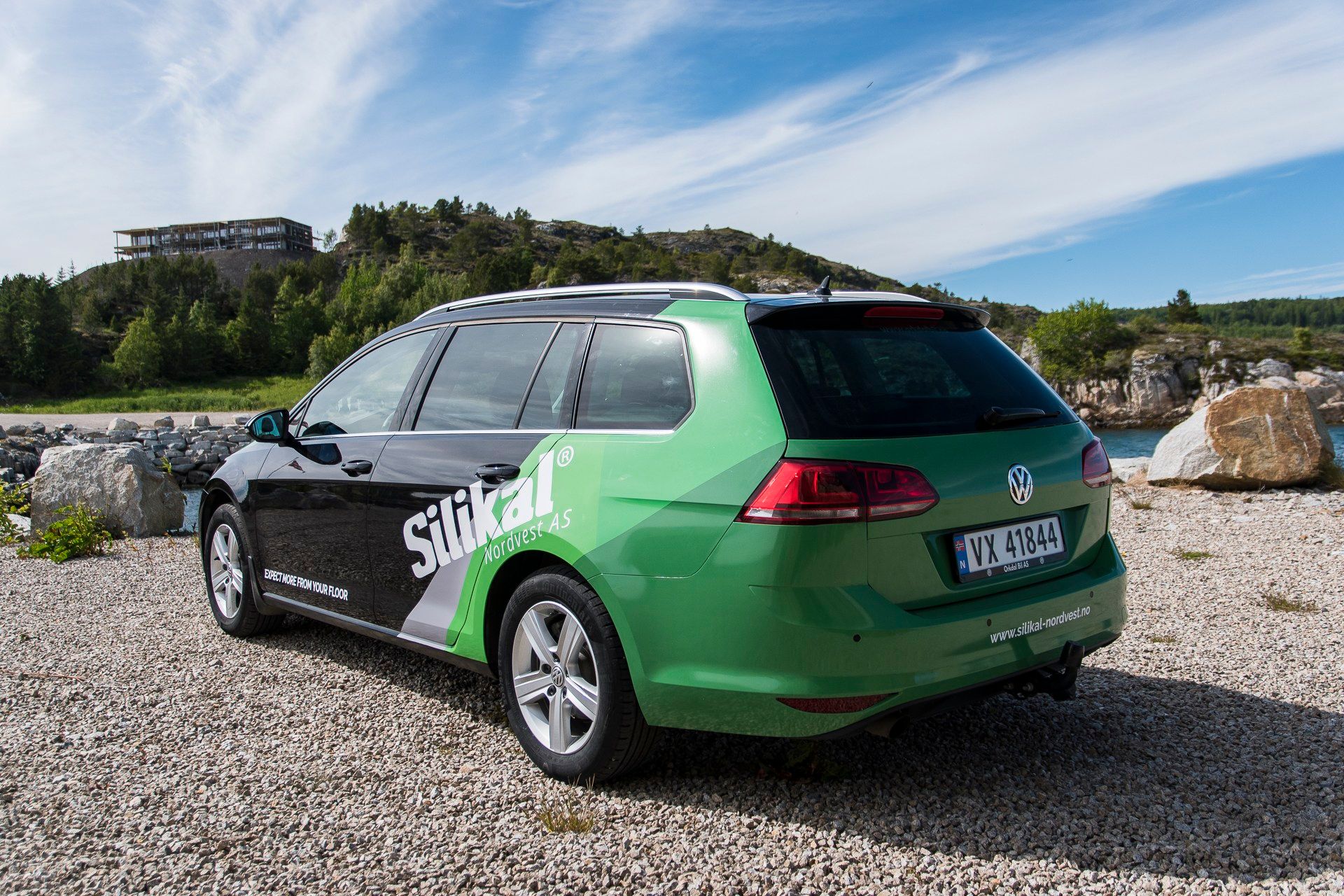 Grønn og sort Volkswagen Golf stasjonsvogn med Silikal-foliering som reklameflate, parkert på grusområde med fjell i bakgrunnen.
