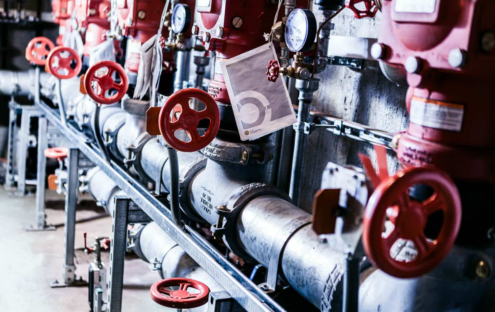 Industrielle rørledninger med røde ventiler og håndhjul montert på metallkonstruksjon.